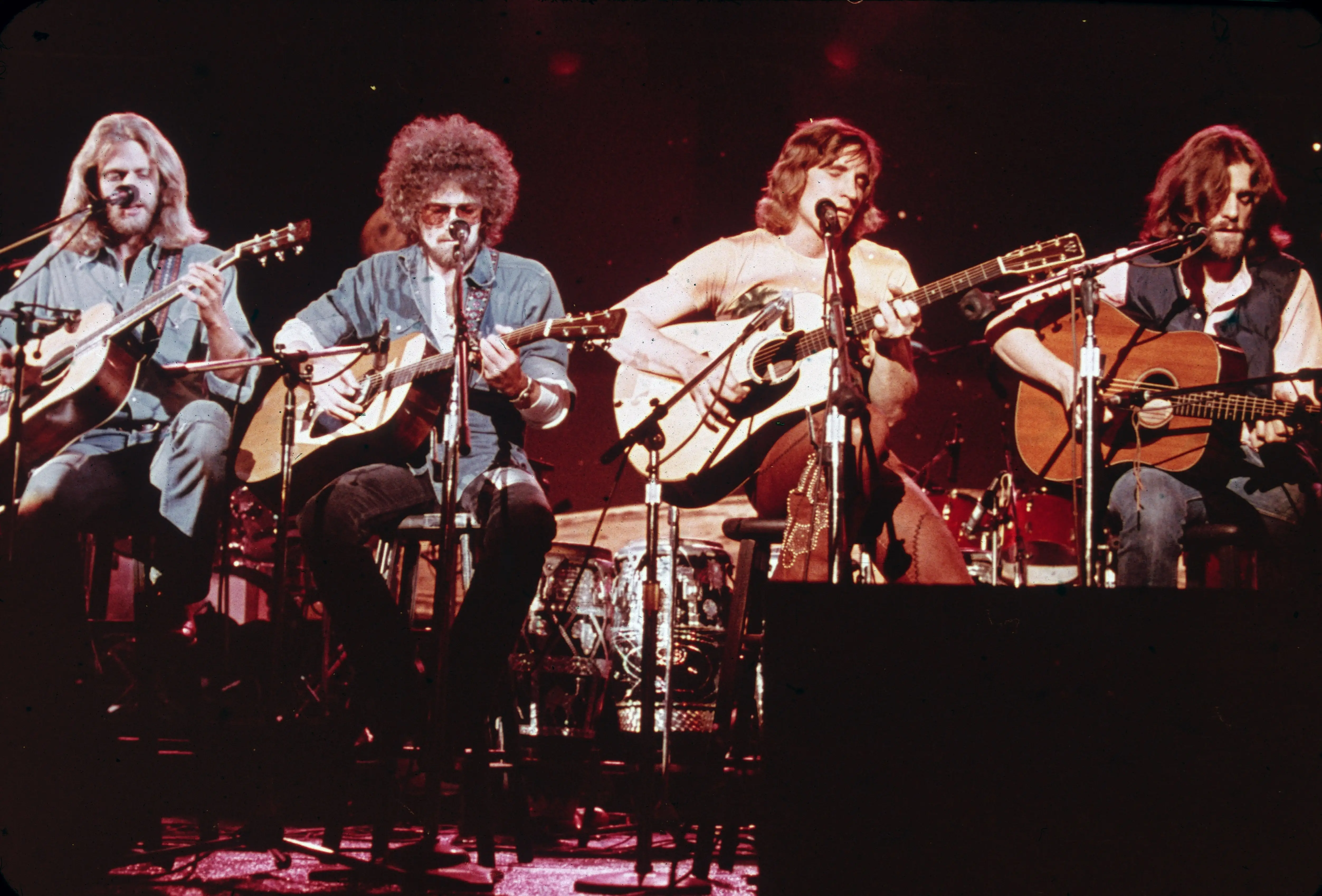 Members of the Eagles sit on stage with acoustic guitars and microphones.