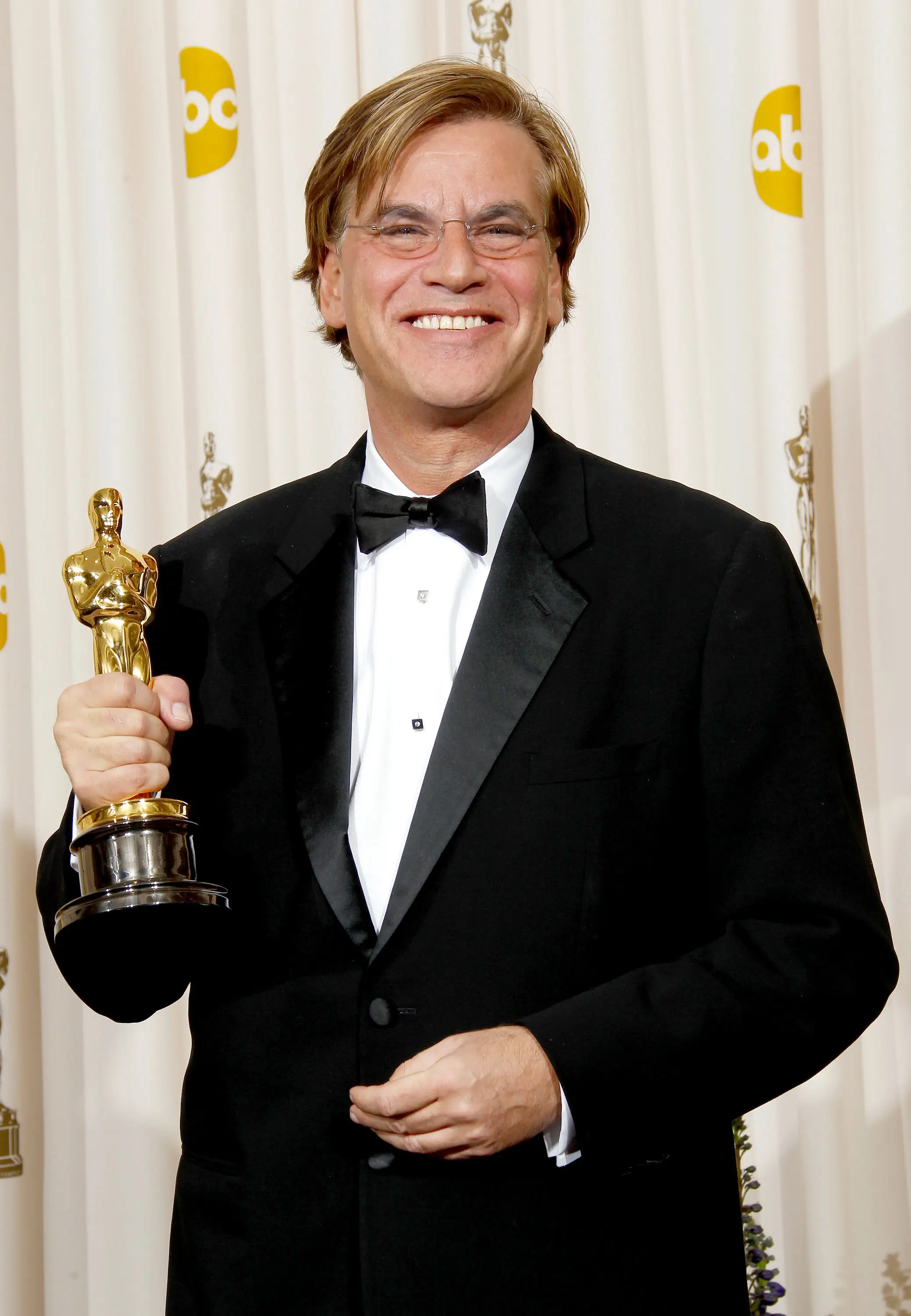 Aaron Sorkin in a tuxedo holding up an Oscar
