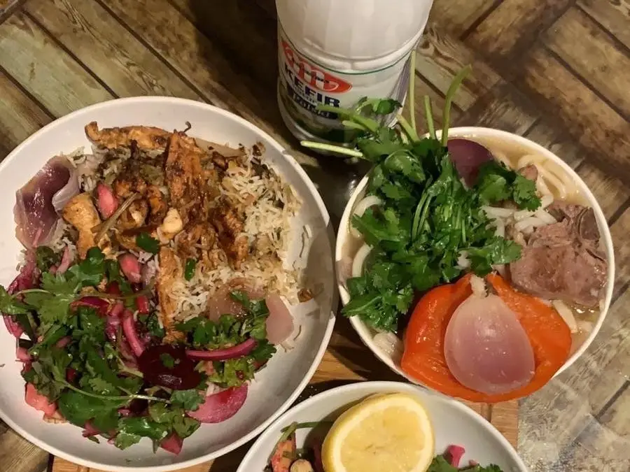 Bowls of rice, salad, vegetables and a dairy drink sit on a wood-patterned table.