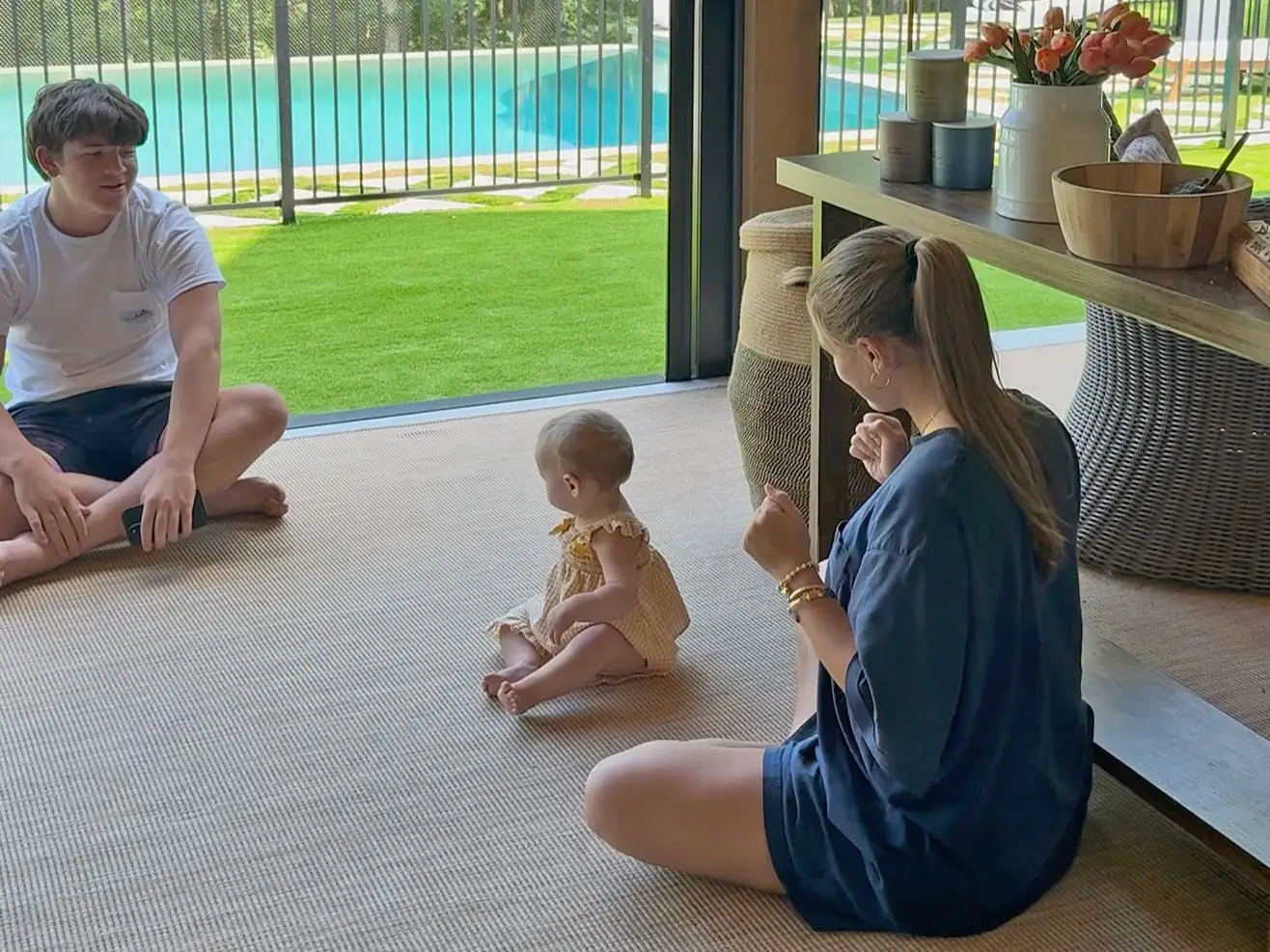 Taylor's younger brother and sister sit on the floor with her daughter.