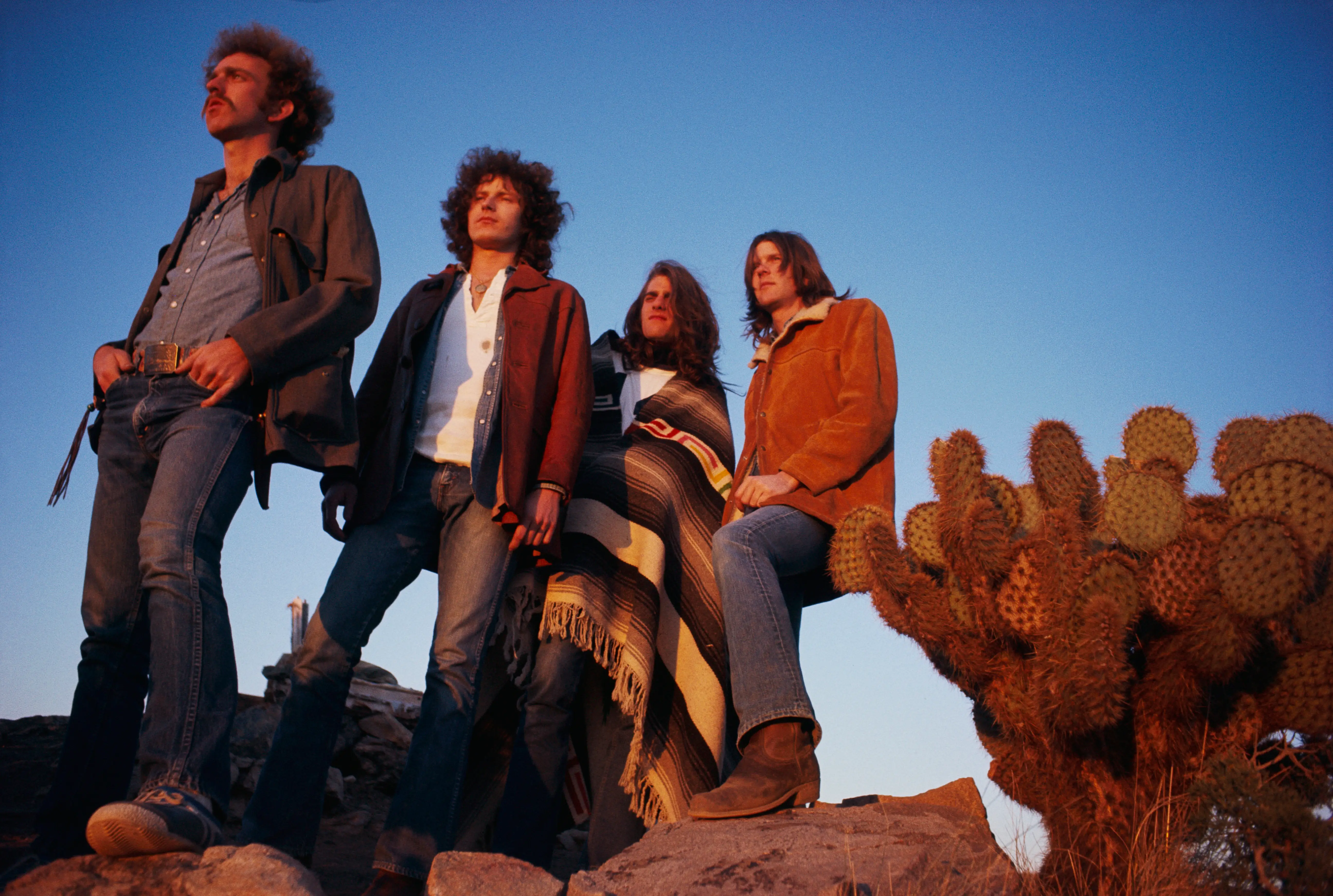 Rock band the Eagles pose in the desert next to a cactus.