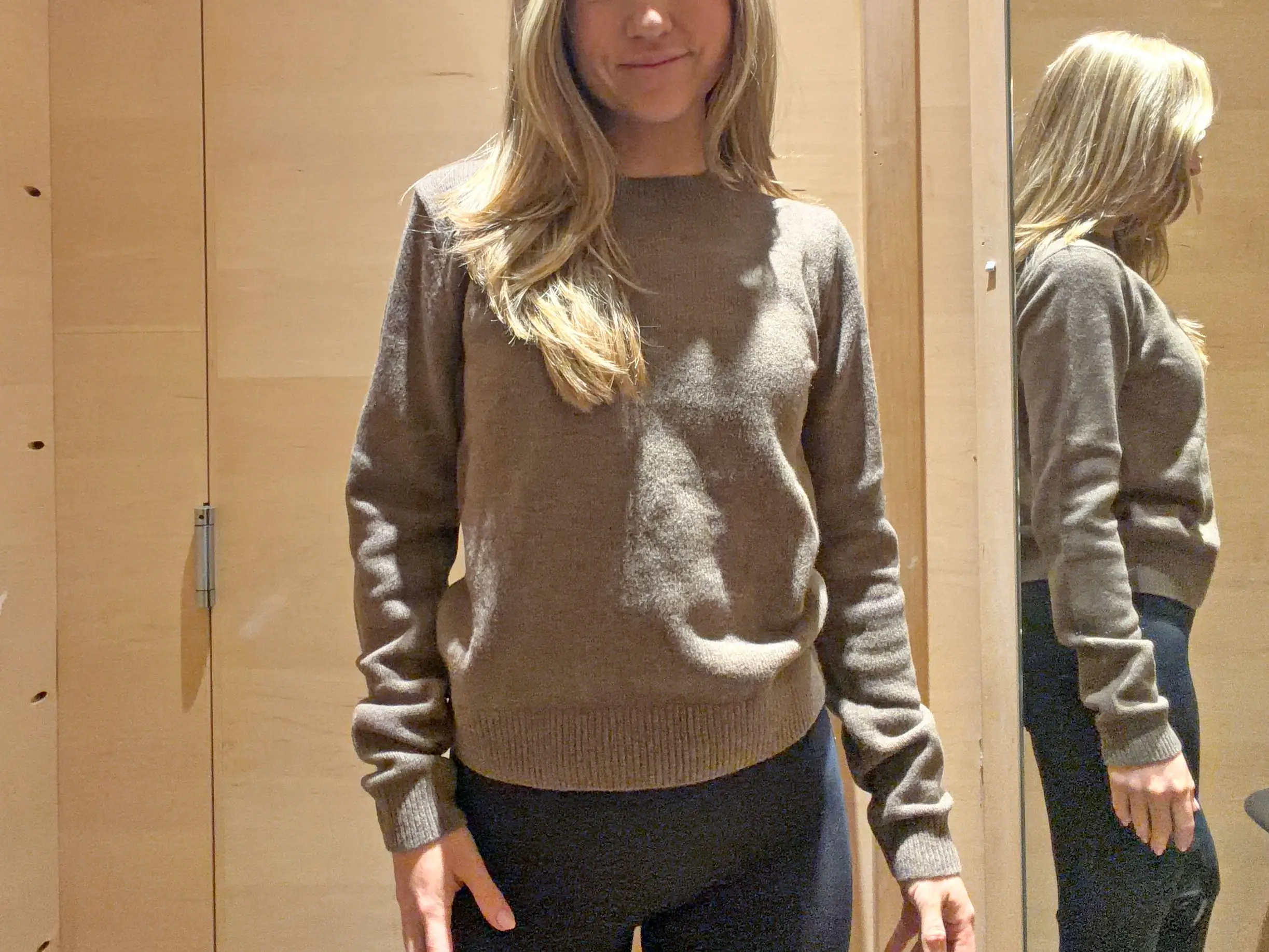 Chloe wears a brown sweater in a fitting room.