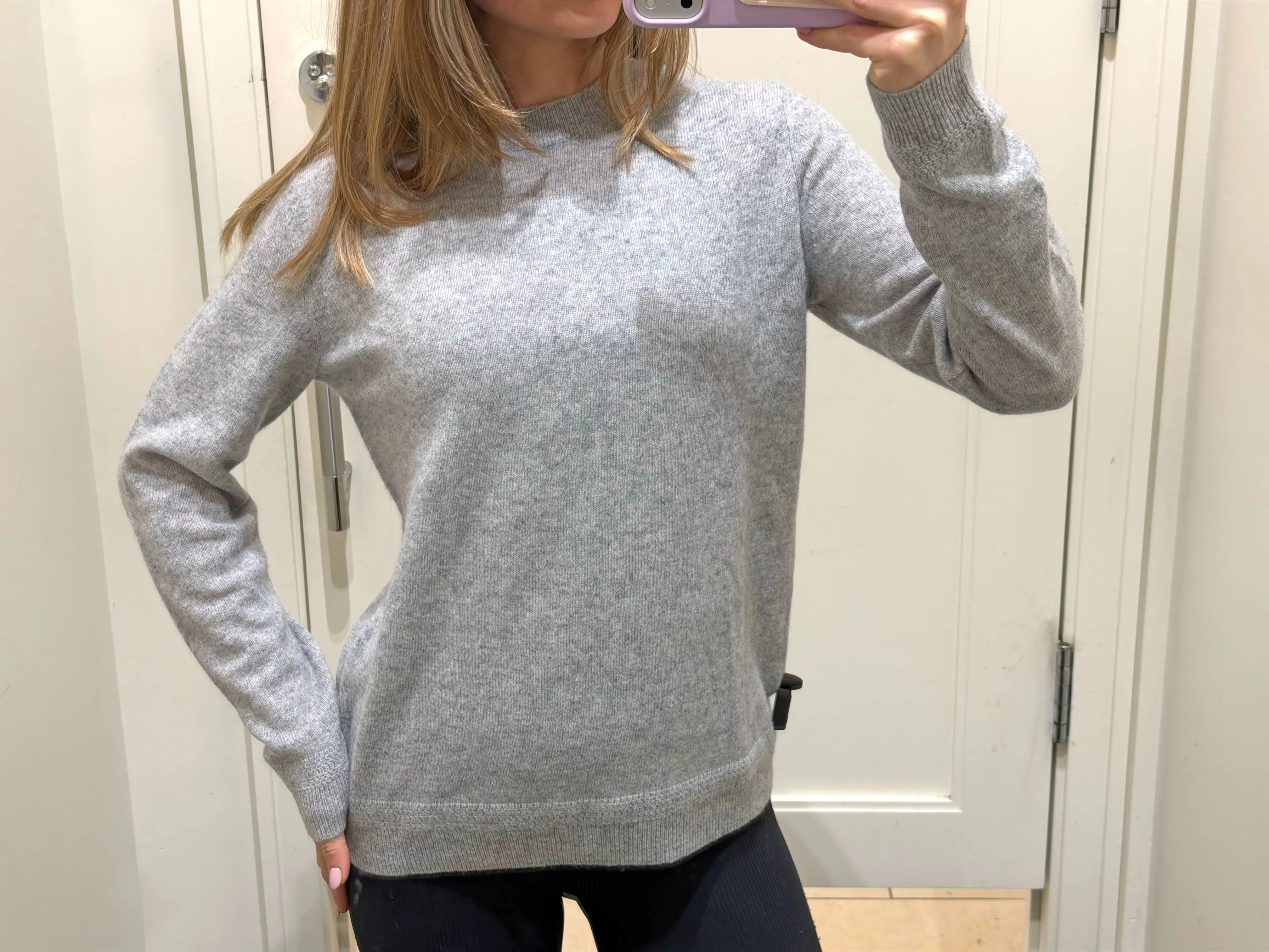 Chloe wears a gray sweater in a fitting room.