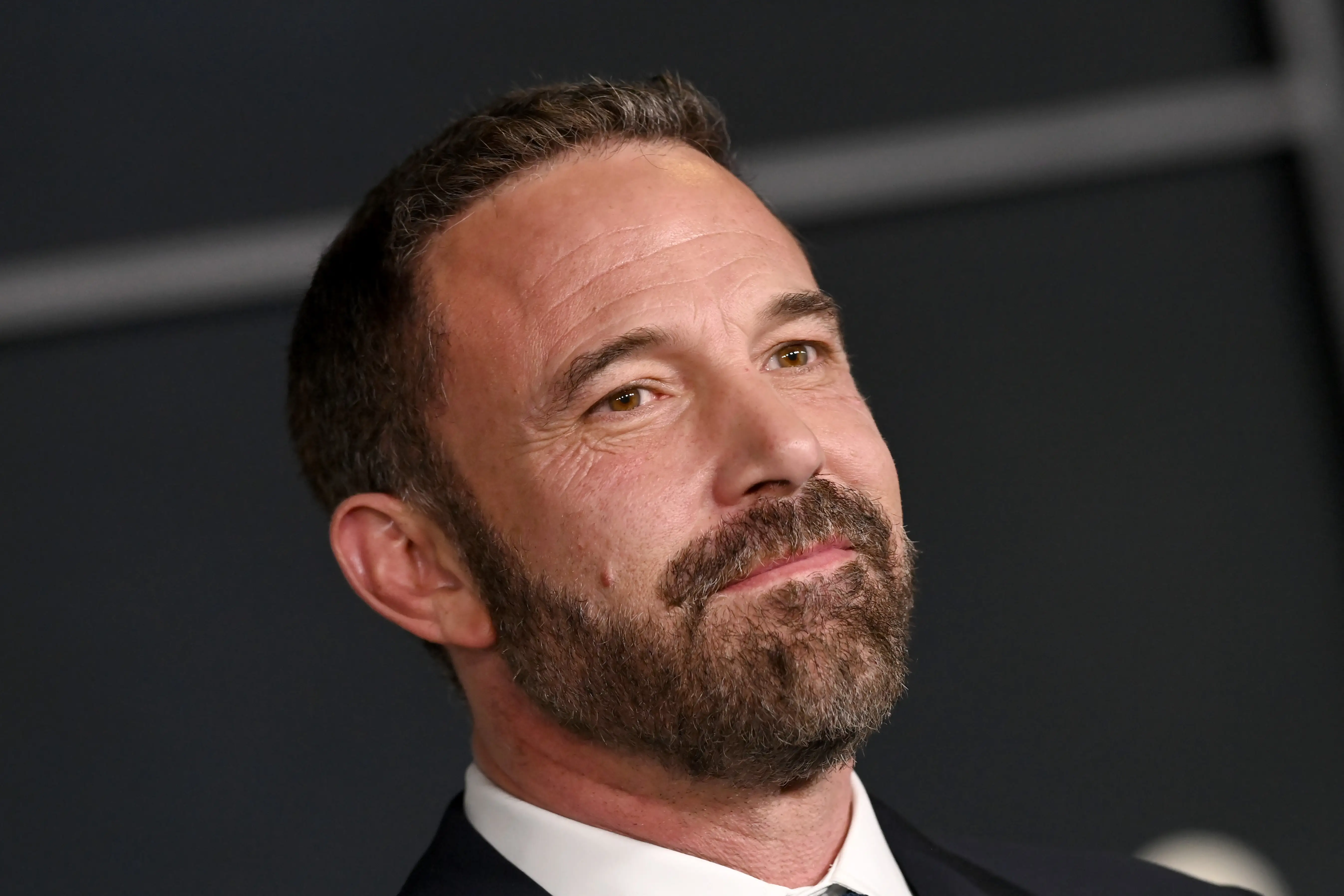 Ben Affleck poses in a close-up portrait against a dark event backdrop.