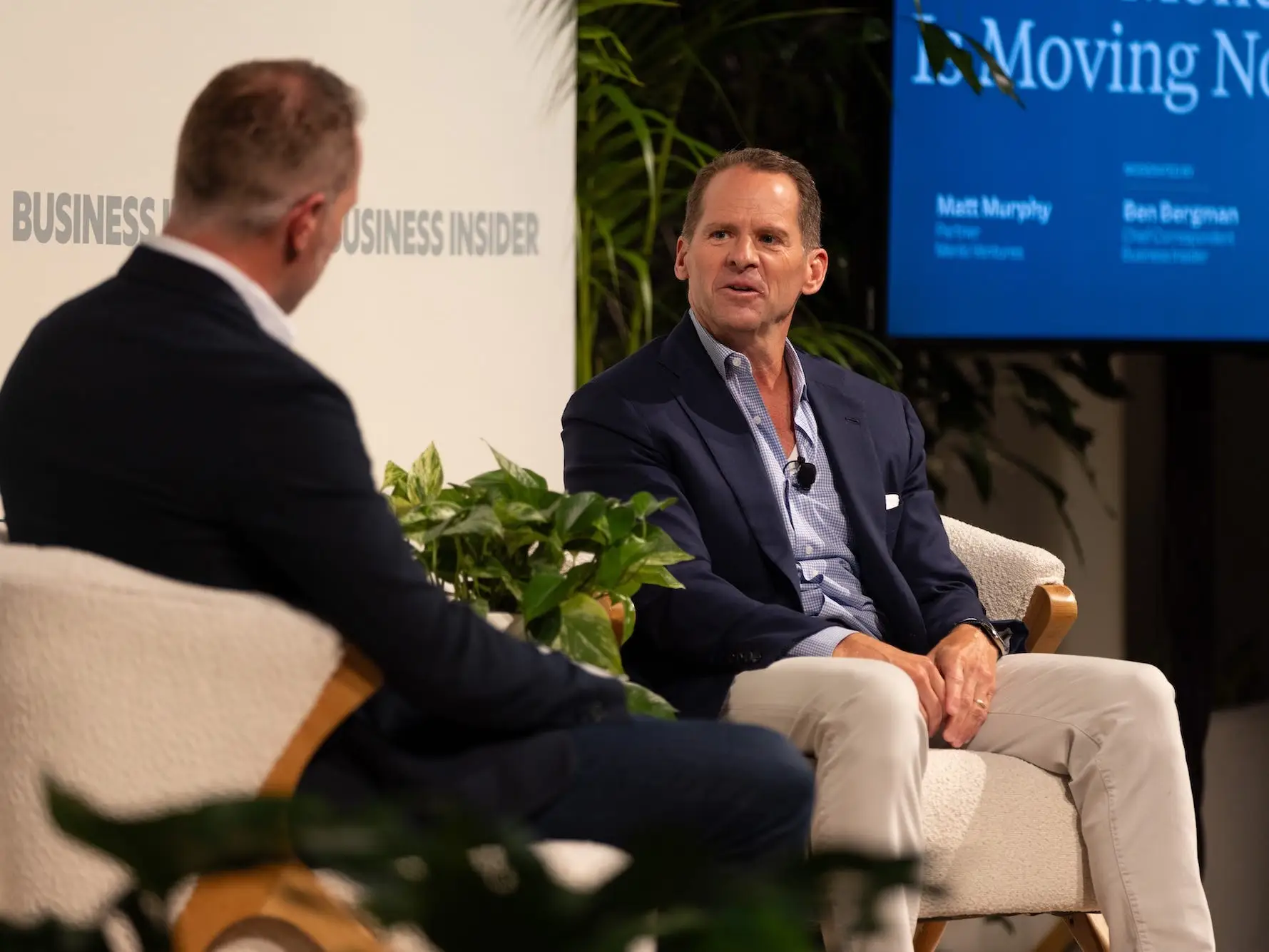 Two people sit onstage during a Business Insider panel discussion with plants and a presentation screen behind them.