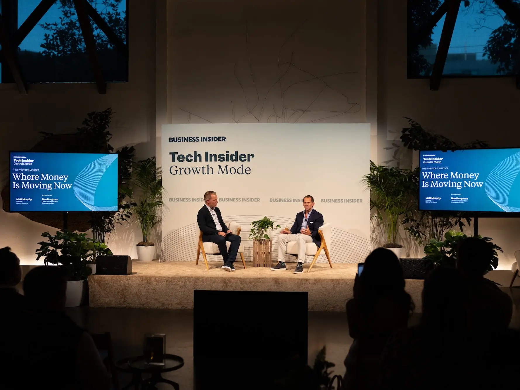 Two people sit onstage during a Business Insider panel discussion with plants and a presentation screen behind them.