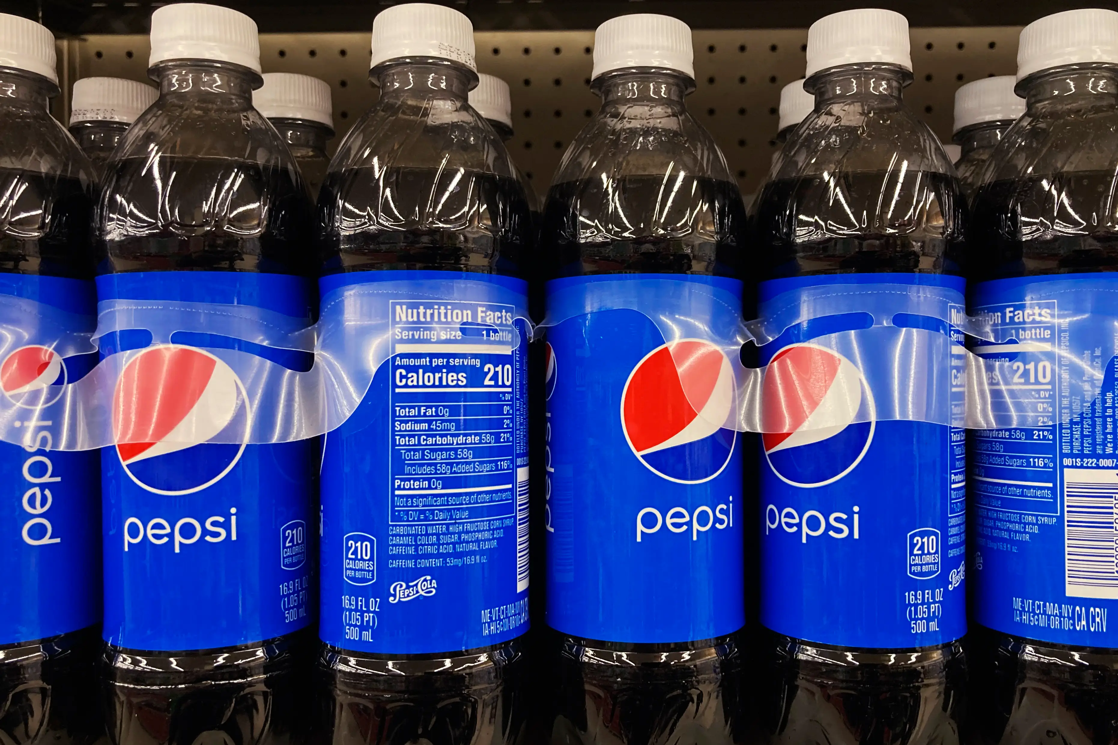 Rows of Pepsi bottles with blue labels and white caps are lined up on a store shelf.