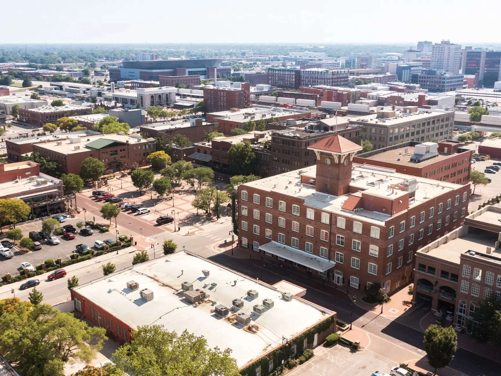 Aerial view of a downtown district with brick buildings, tree-lined streets, parking lots, and a clock tower.