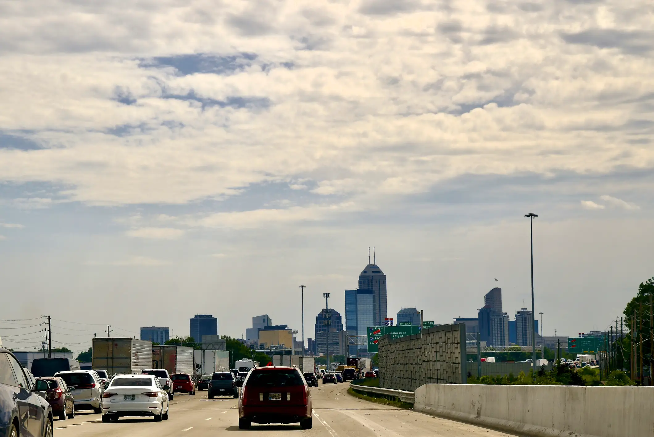 Traffic moves along a highway toward a downtown skyline under a cloudy sky.