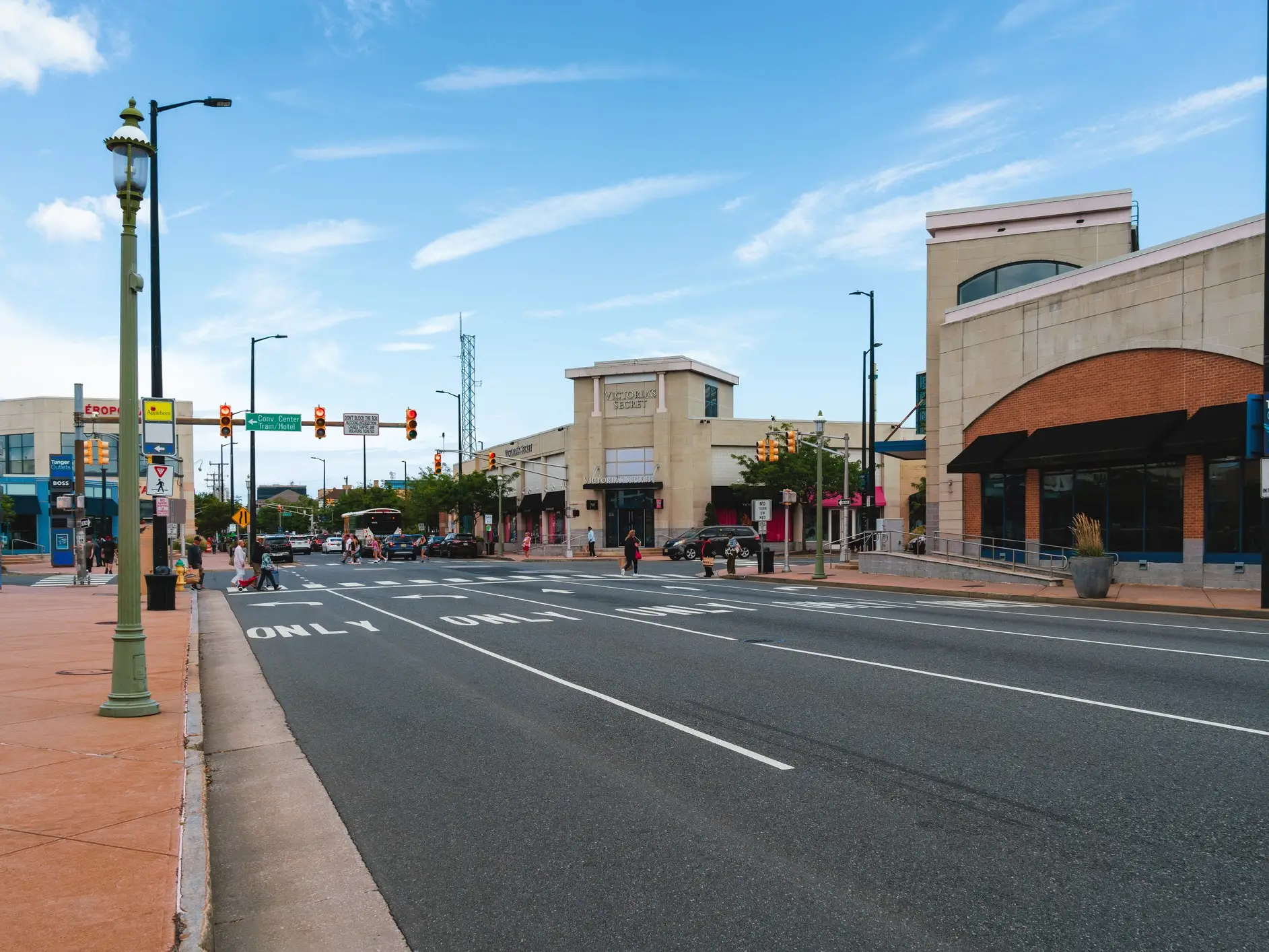 Wide city street with traffic signals, pedestrians, and storefronts including Target and VICTORIA'S SECRET PINK under blue sky.
