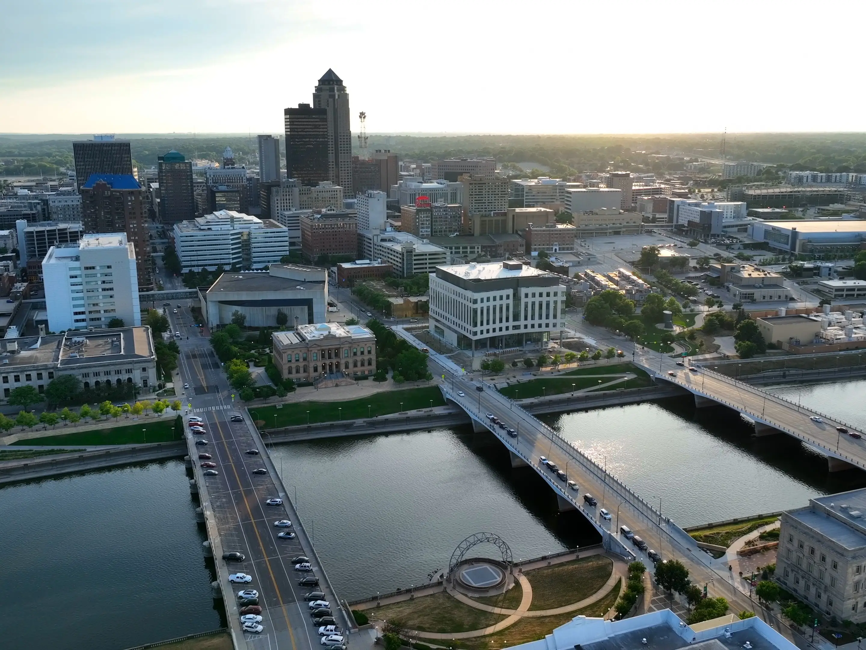Aerial view of downtown Des Moines skyline, river bridges, and traffic at sunset.