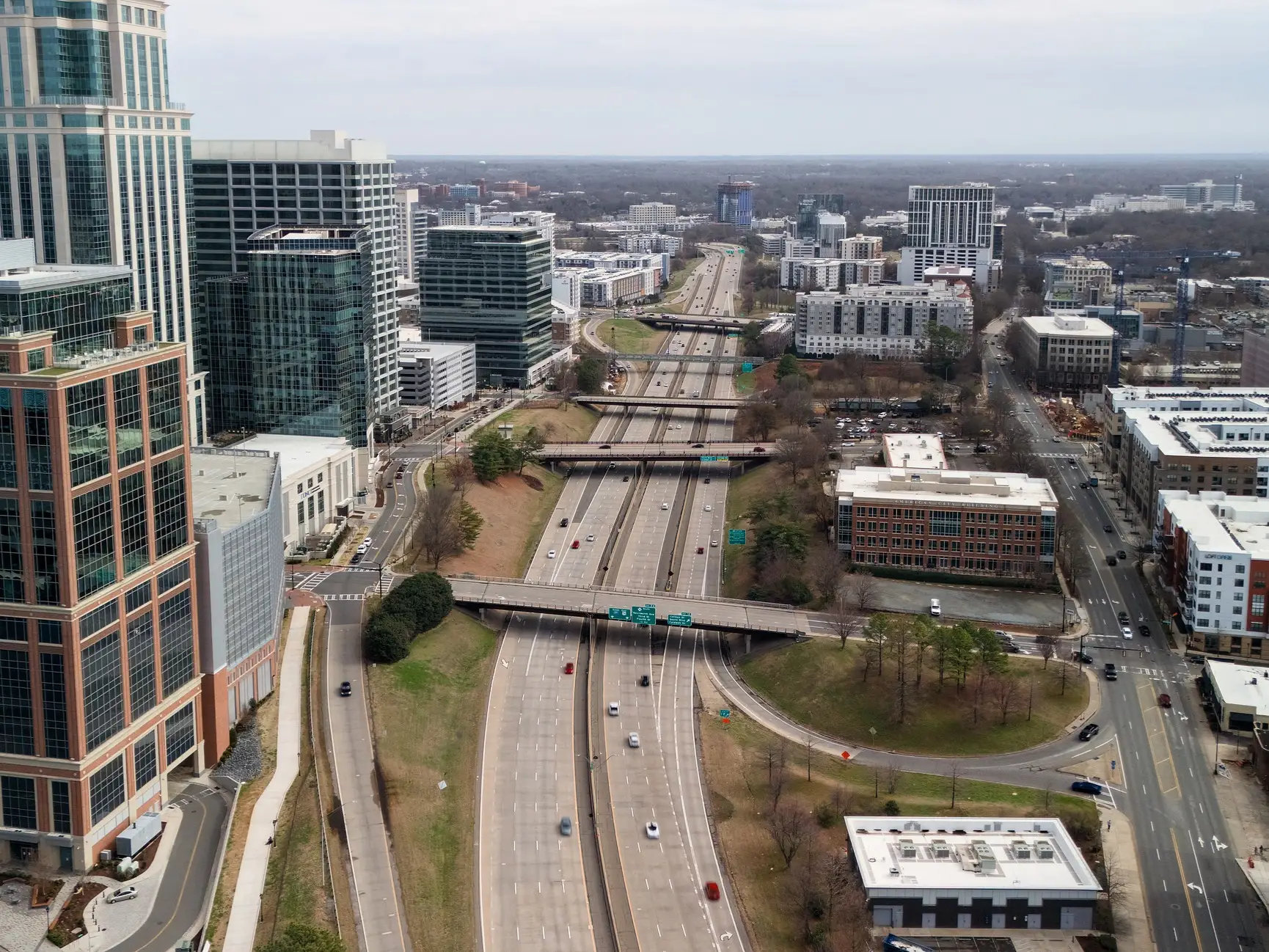 Aerial view of a multilane highway running through a downtown area with office towers and surrounding streets.