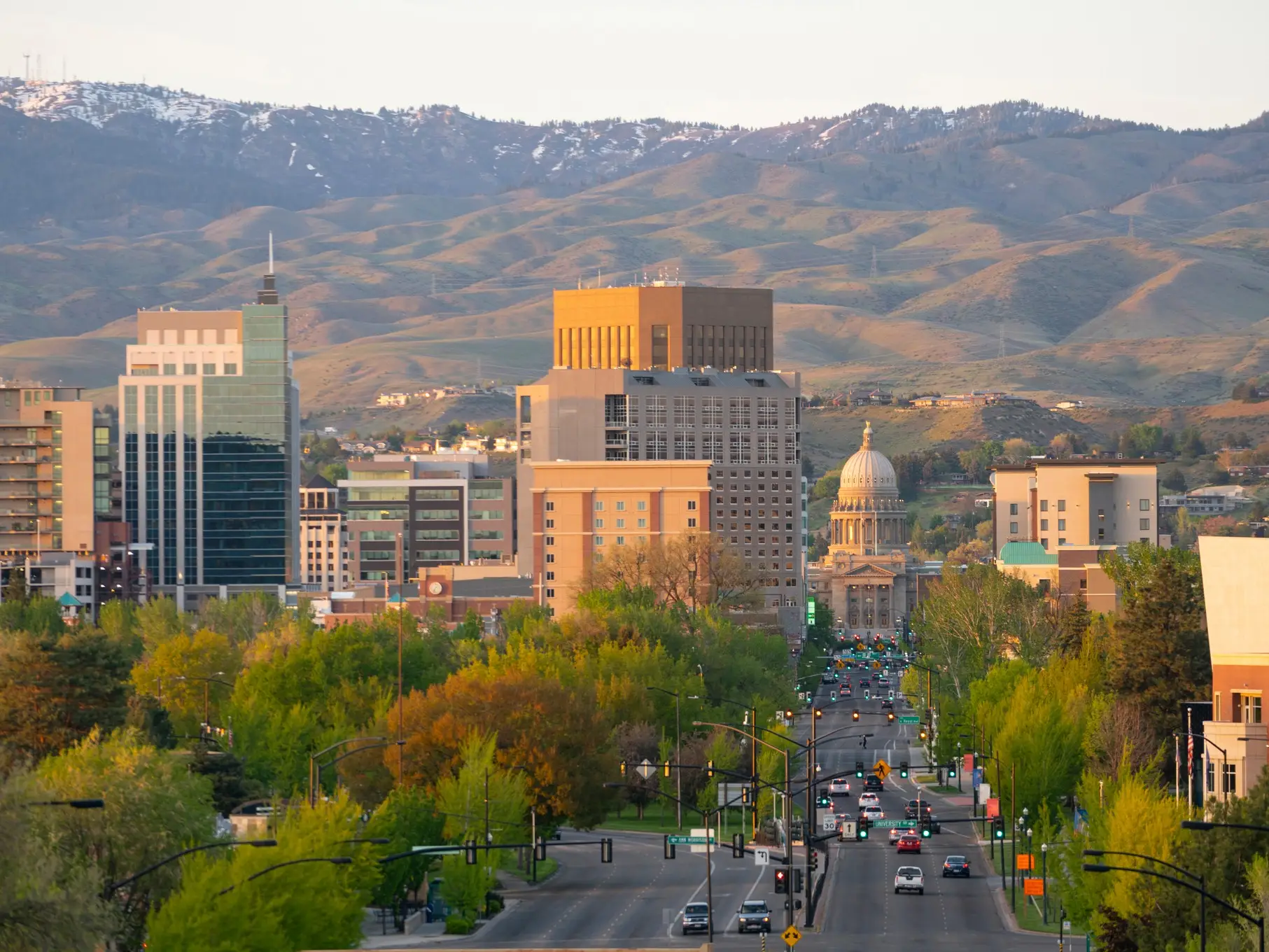 Downtown Boise skyline with the Idaho State Capitol and tree-lined streets below foothills at golden hour.