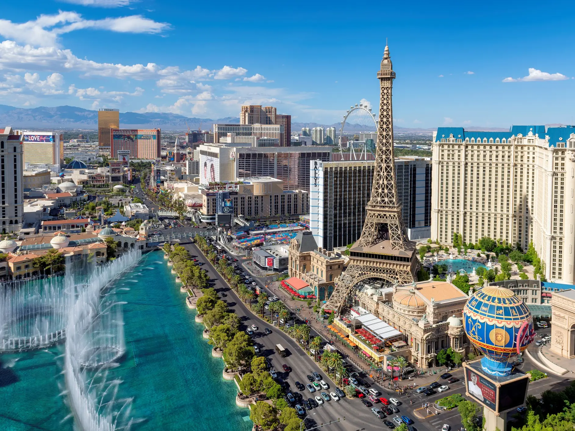 Las Vegas Strip skyline with Paris Las Vegas Eiffel Tower, Bellagio fountains, and hotel towers under a blue sky.