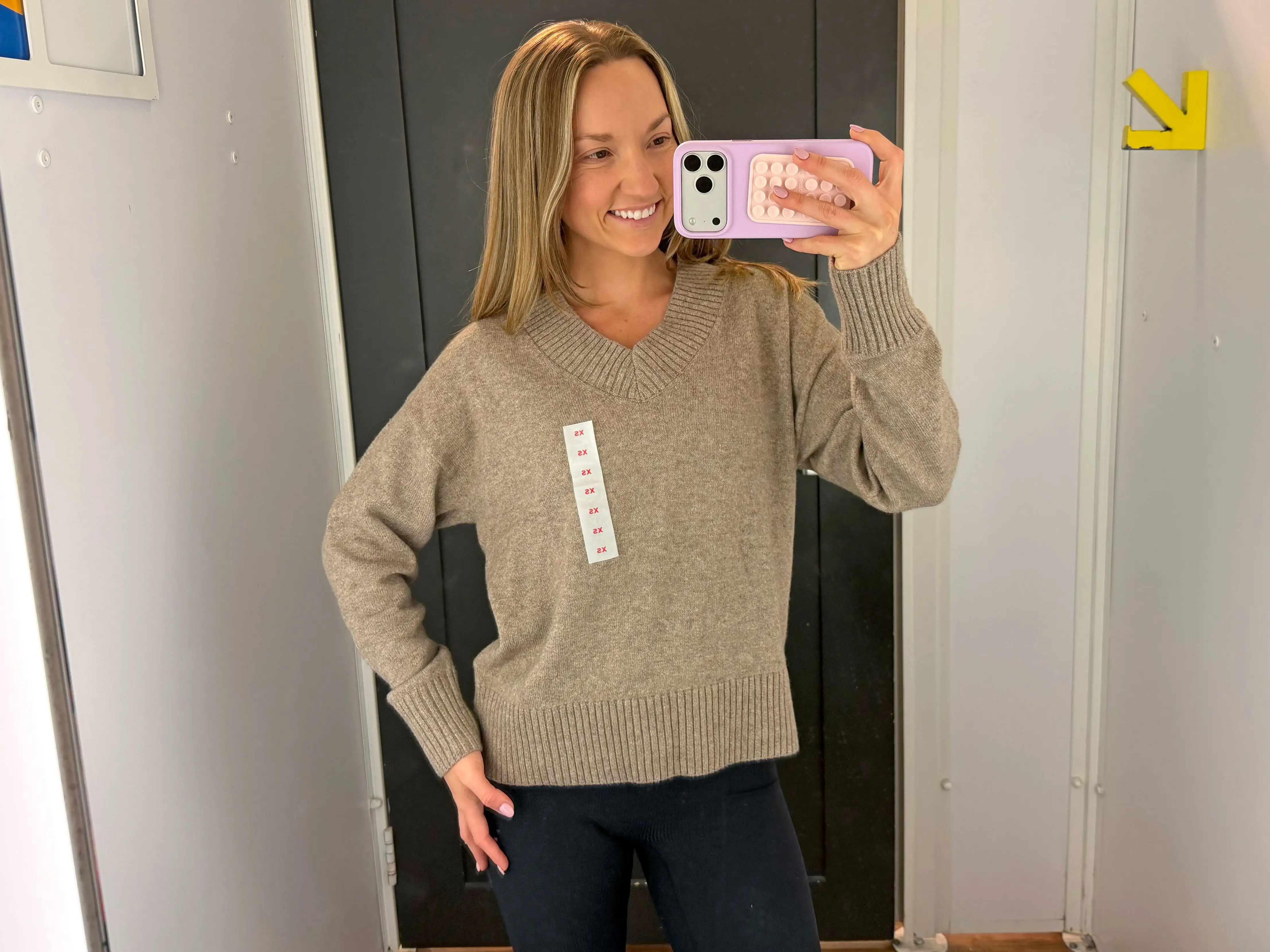 Chloe wears a beige, V-neck sweater in a fitting room.