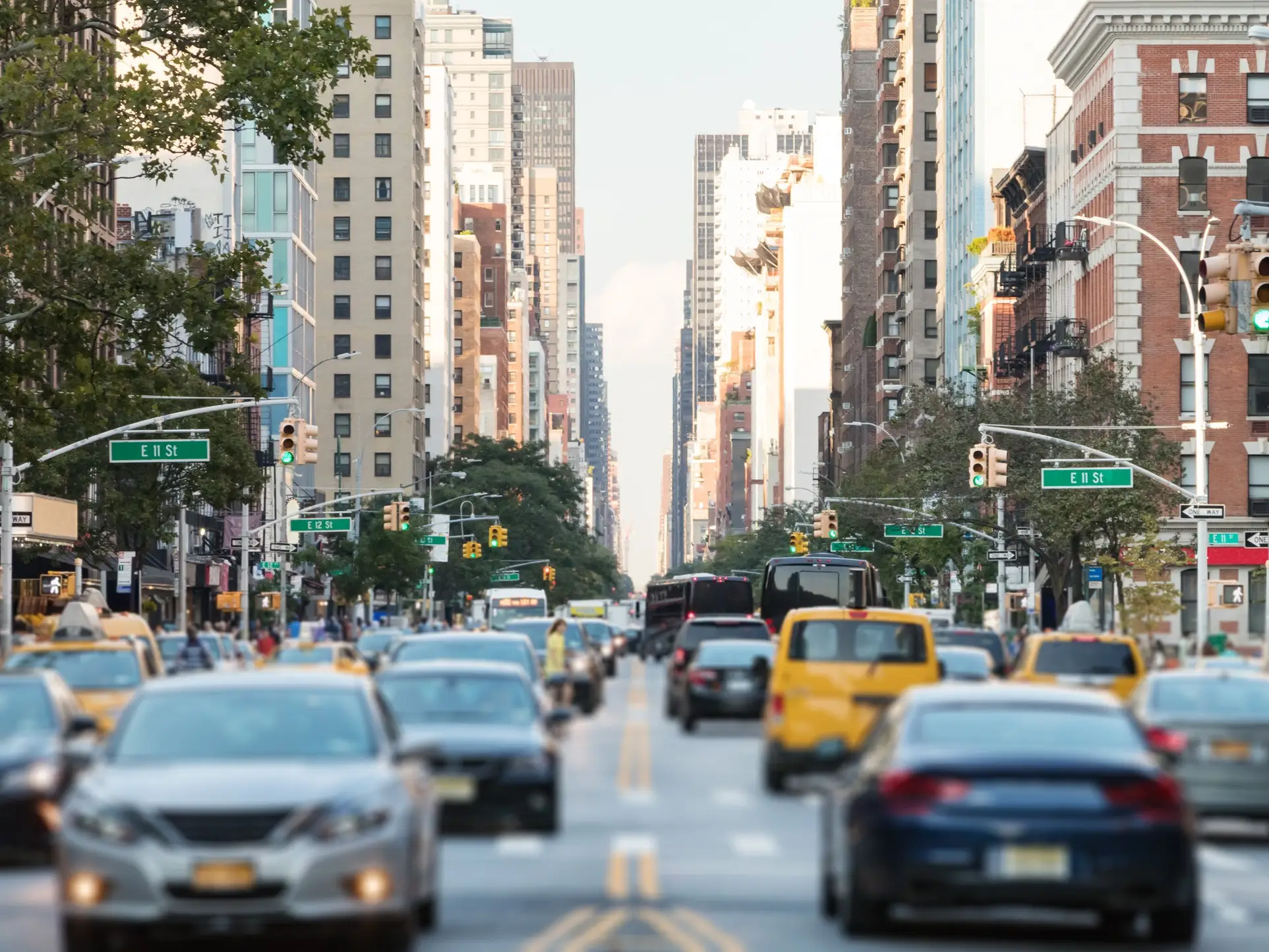 Traffic fills a broad urban avenue lined with tall buildings and visible E 11 St and E 12 St signs.