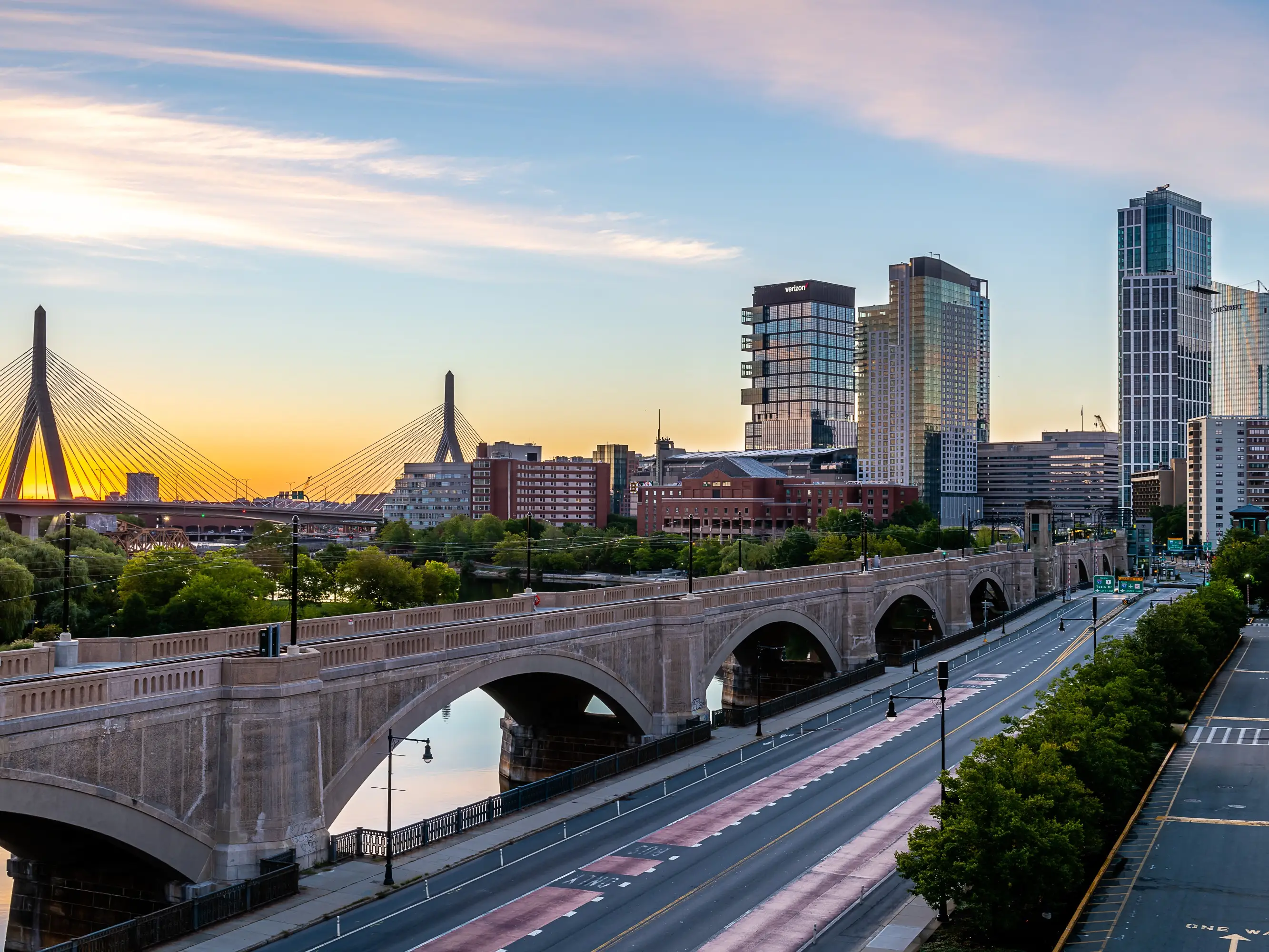Boston skyline at sunset with the Longfellow Bridge, Charles River, and Zakim Bridge visible in the distance.