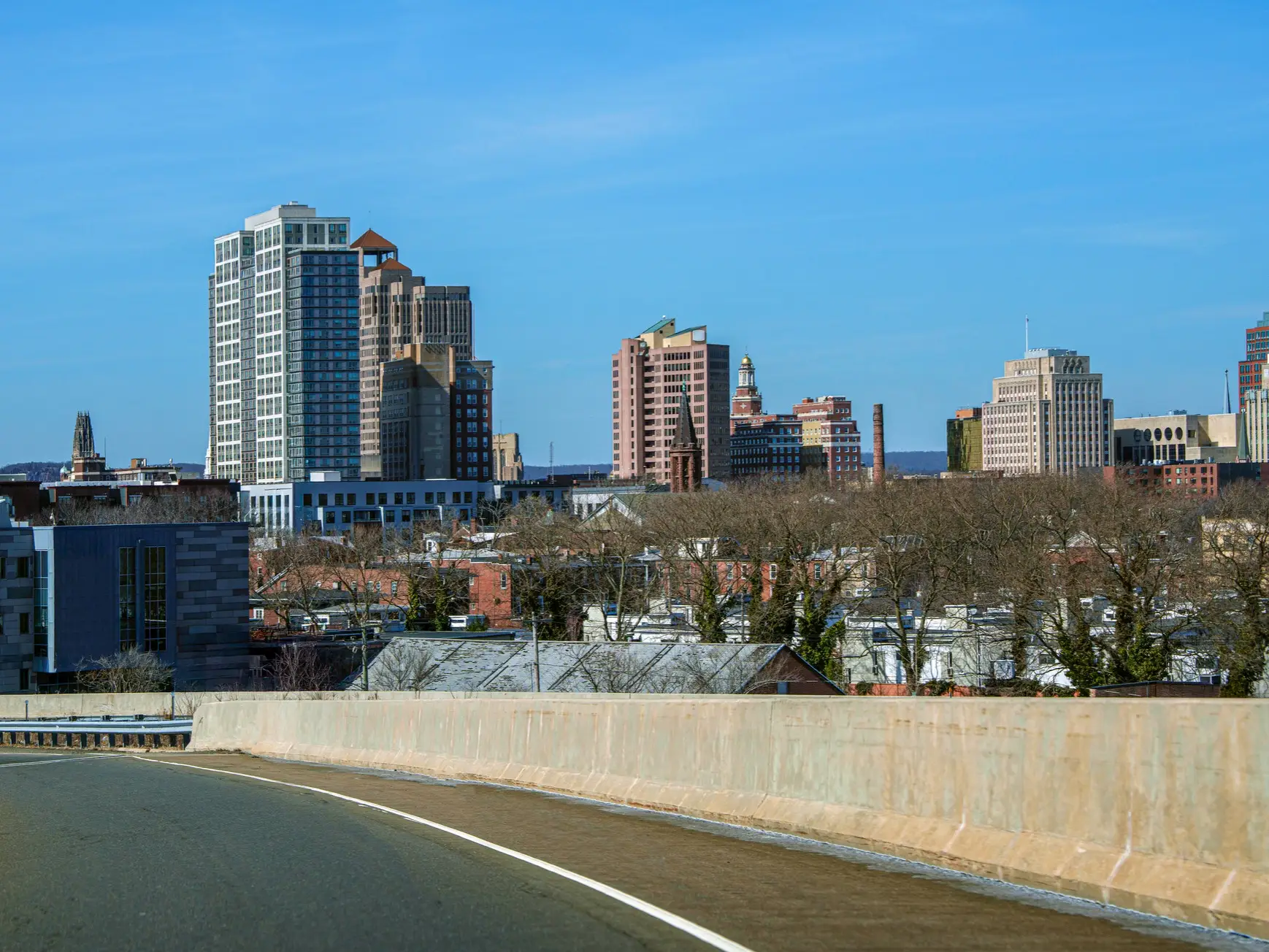 New Haven skyline rises beyond an elevated roadway under a clear blue sky.