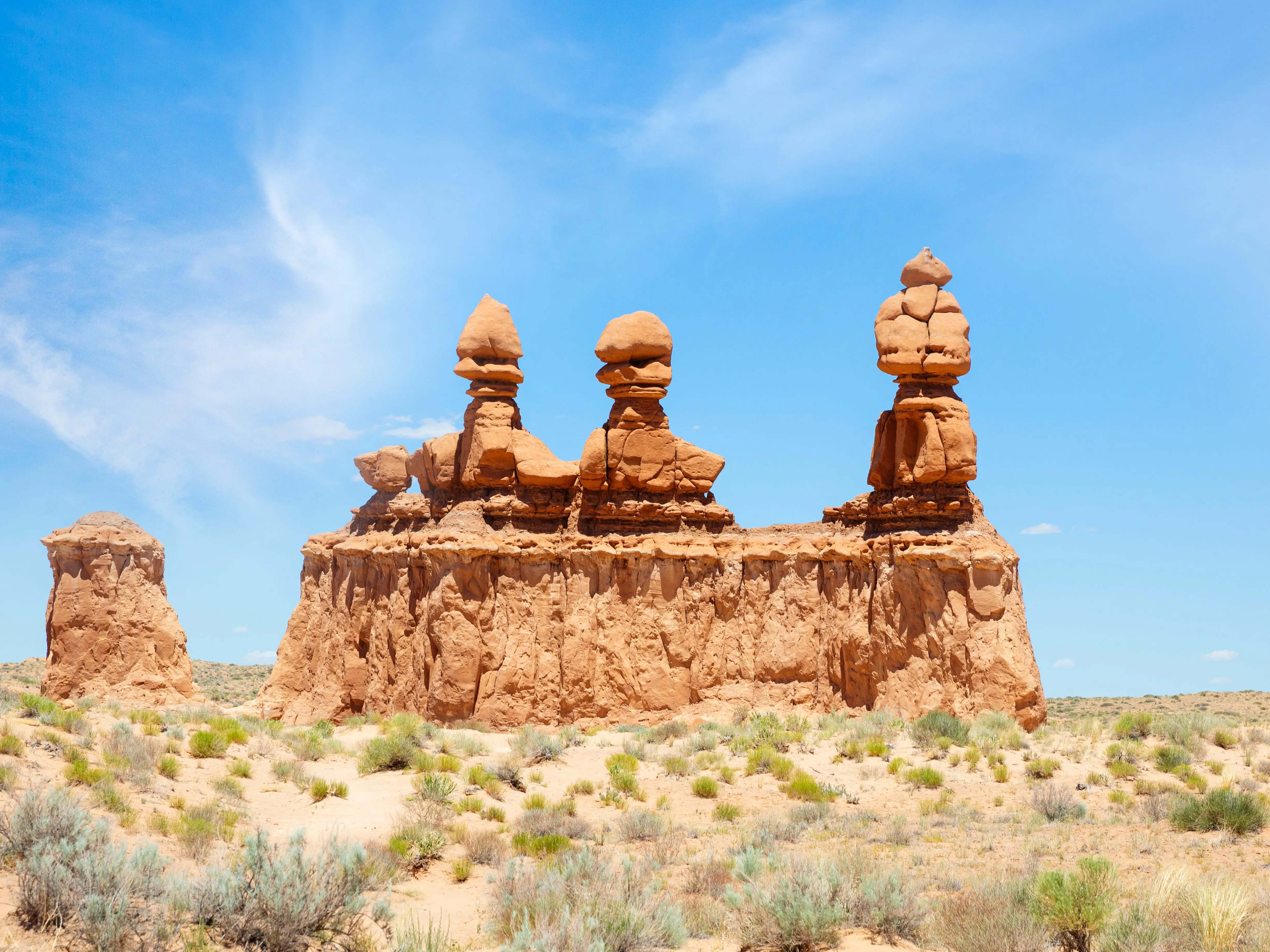 Unique rock formations rise from a desert landscape beneath a bright blue sky in Goblin Valley State Park.