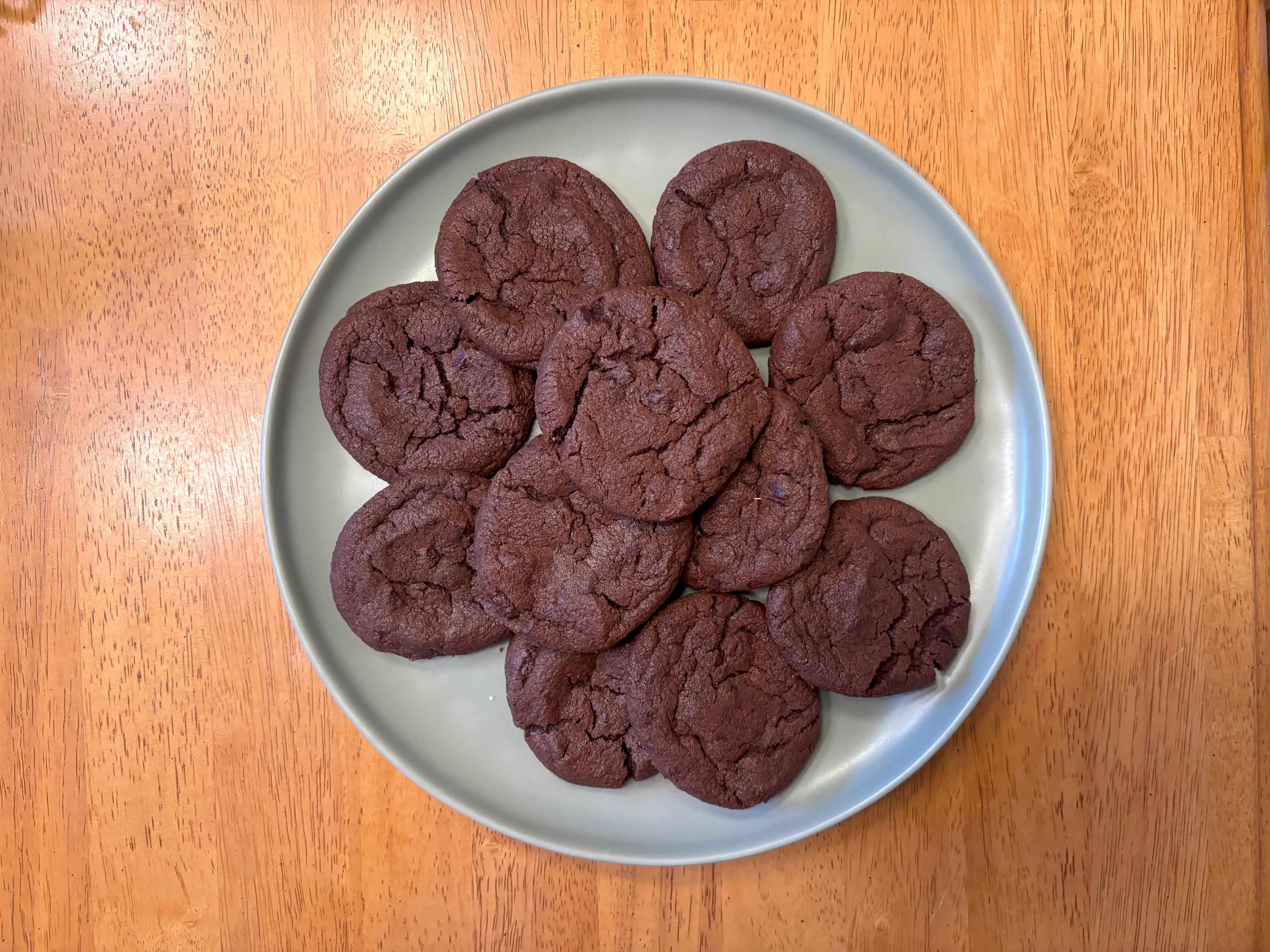 Chocolate cookies are arranged on a green plate atop a wooden table.