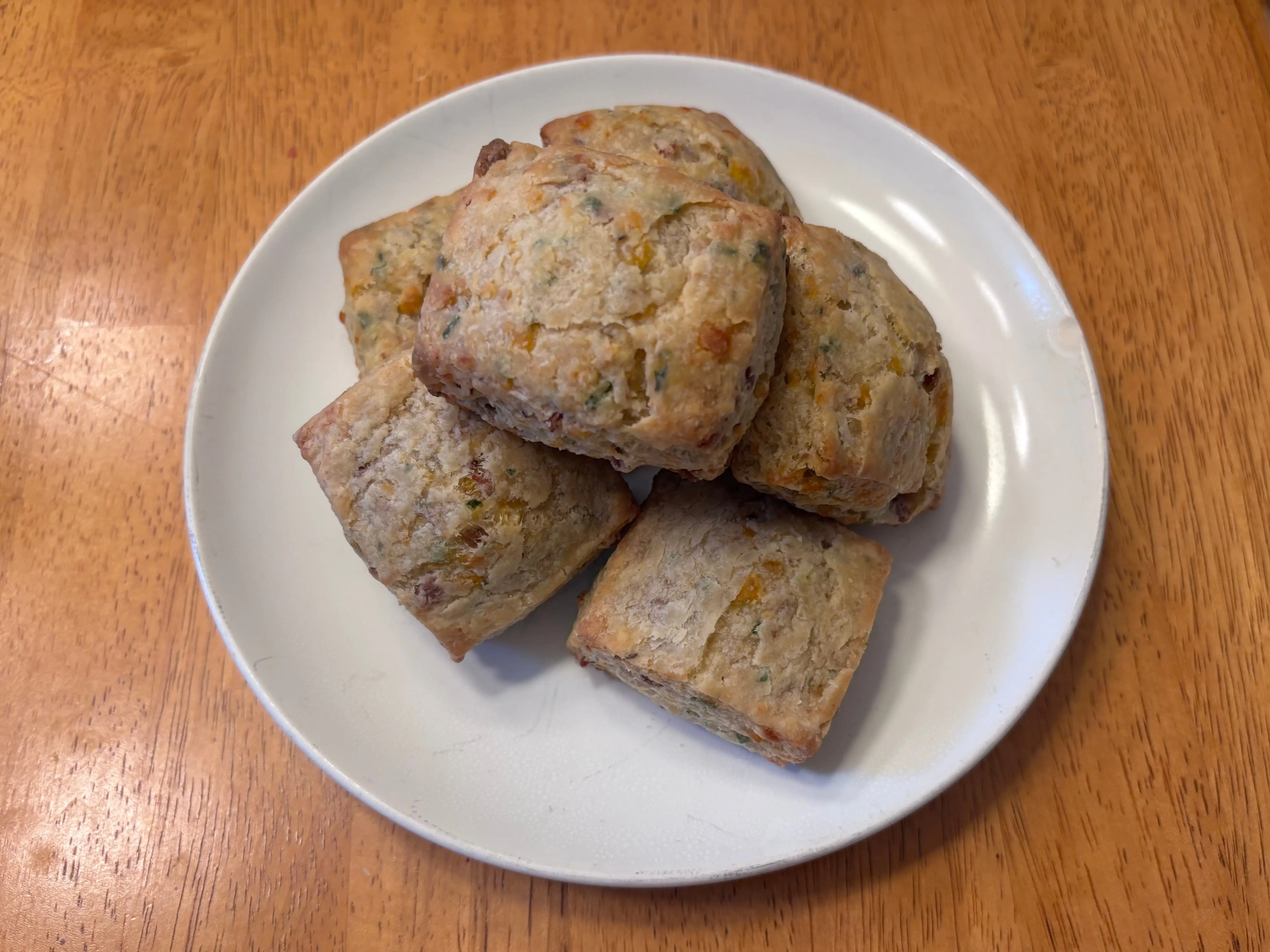 Several square baked biscuits sit stacked on a white plate on a wooden tabletop.