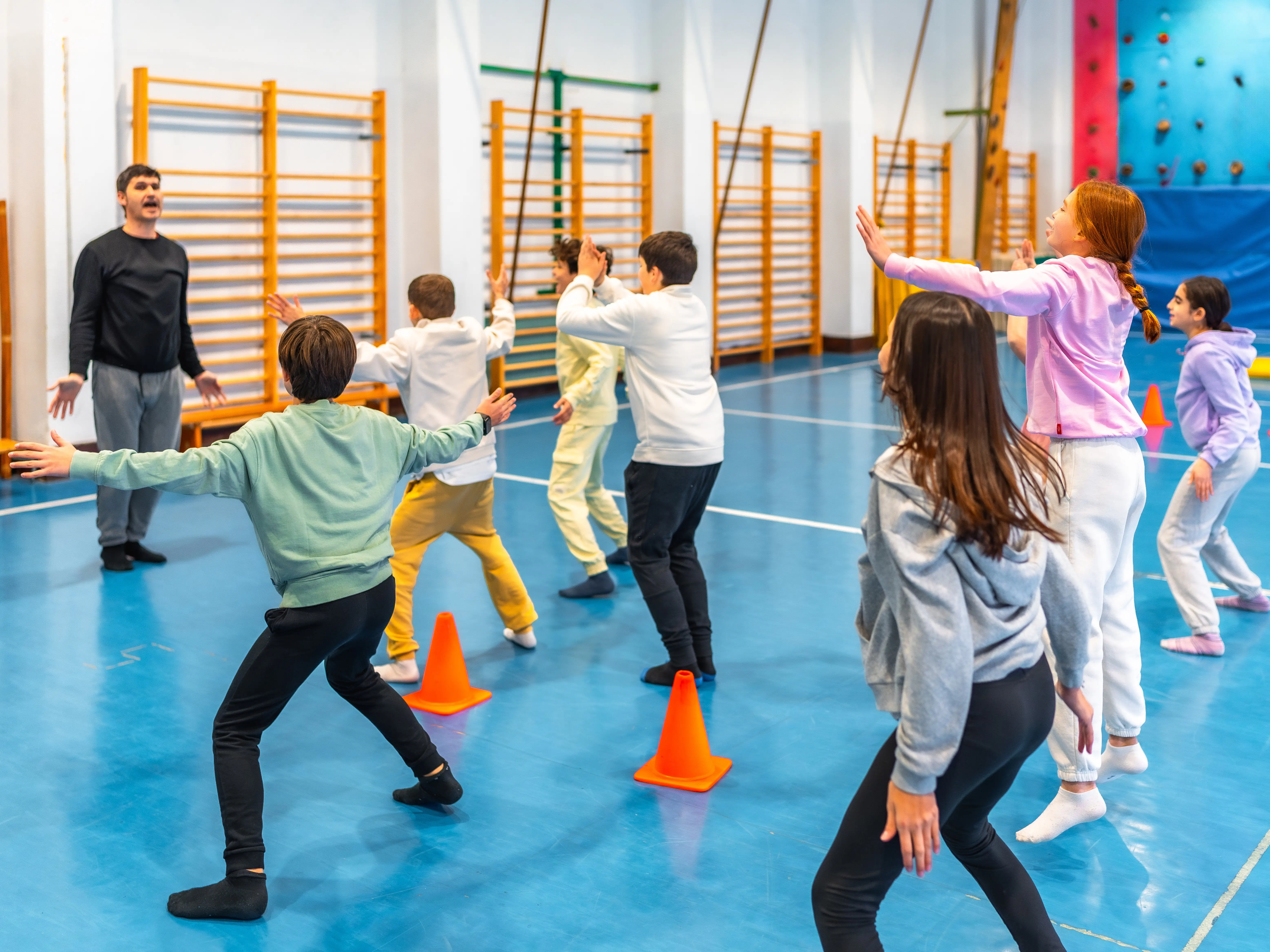 Elementary school students practicing gymnastics exercises with their teacher in the school gym