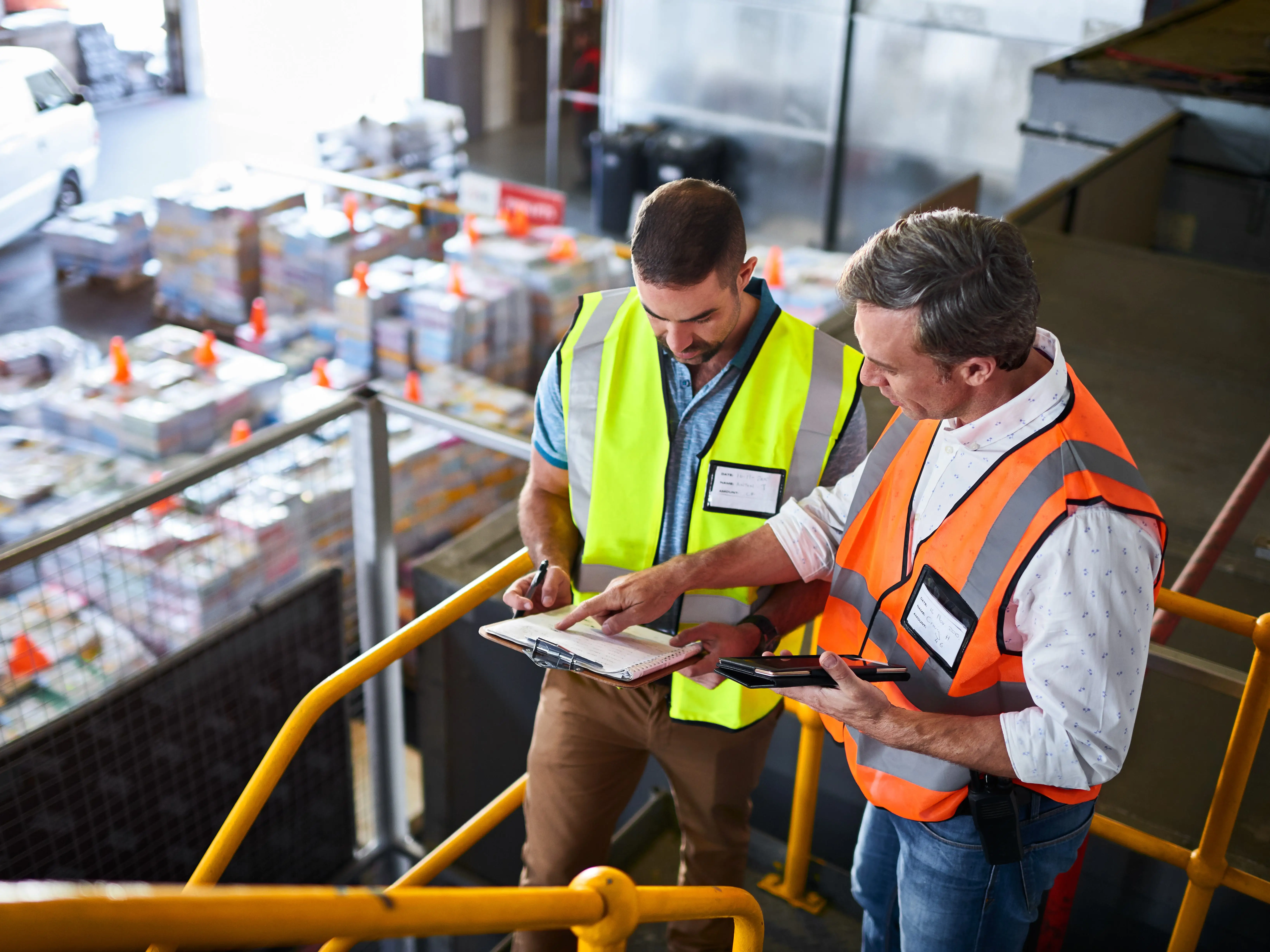 Shot of two warehouse workers standing on stairs using a digital tablet and looking at paperwork