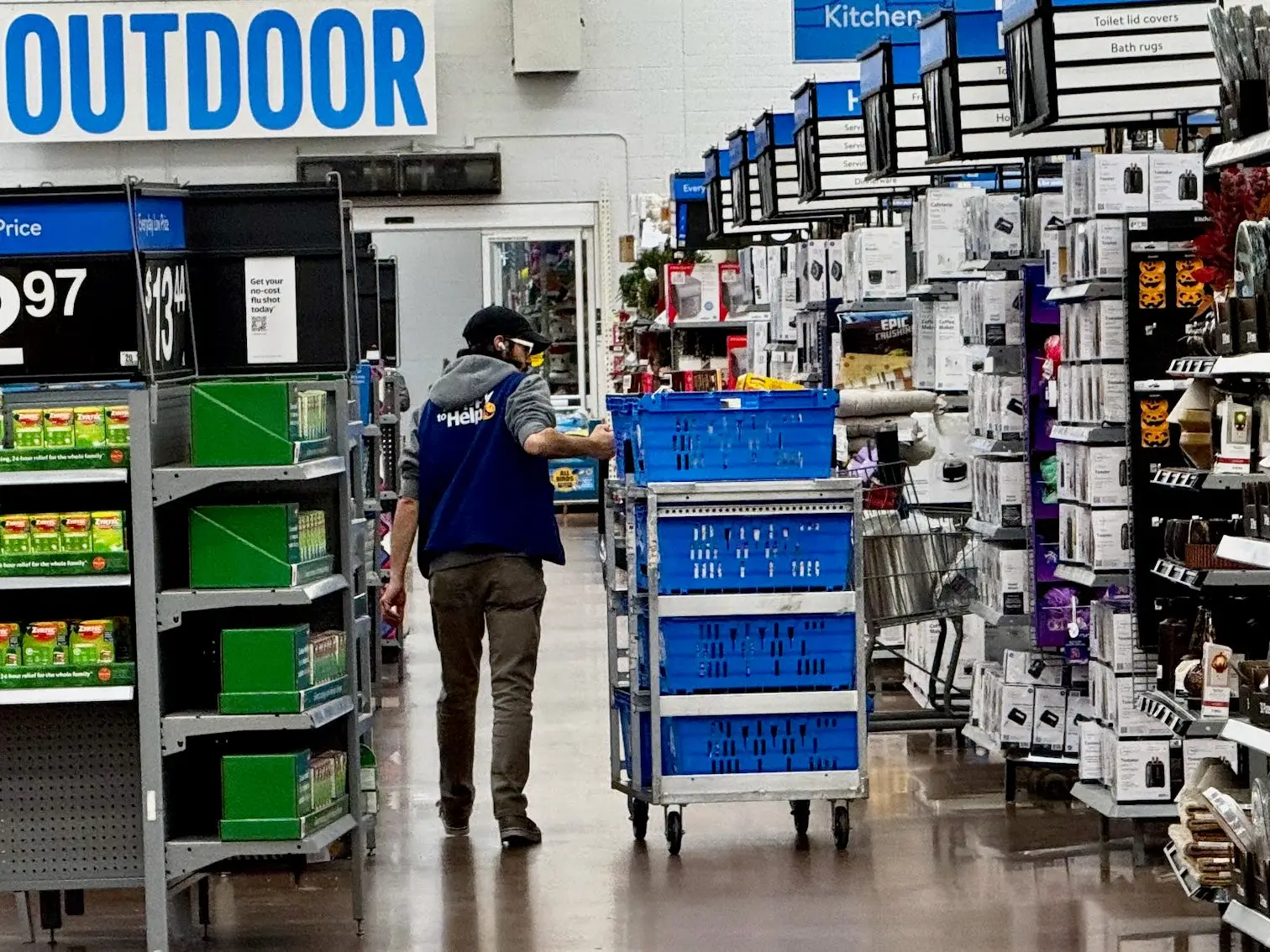 A store employee pushes blue bins through a Walmart aisle near outdoor, bath, and seasonal candy displays.