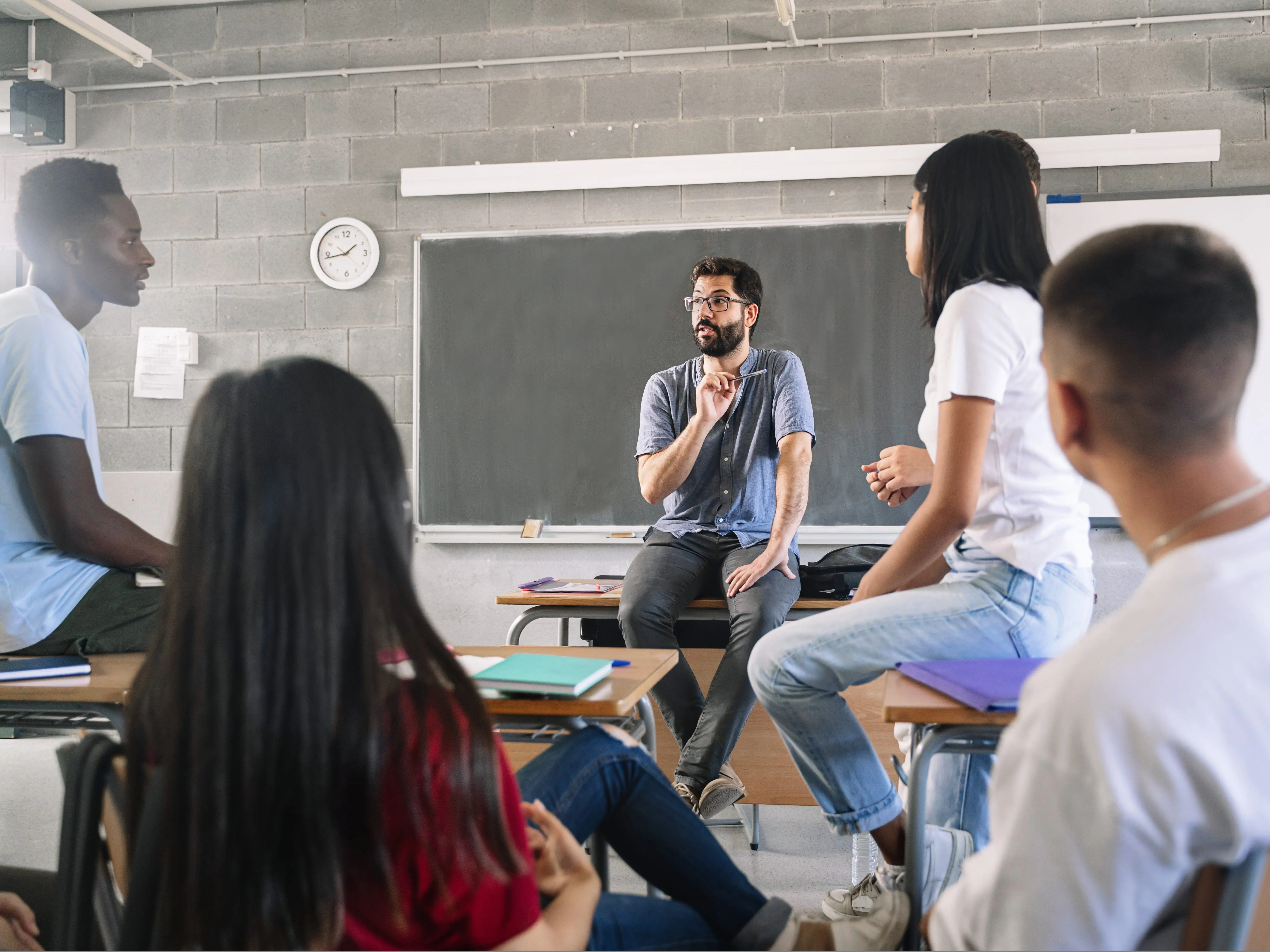 Teenager Teenager students listening and talking to friendly young male teacher - Group discussion in High School Education listening and talking to friendly young male teacher stock photo