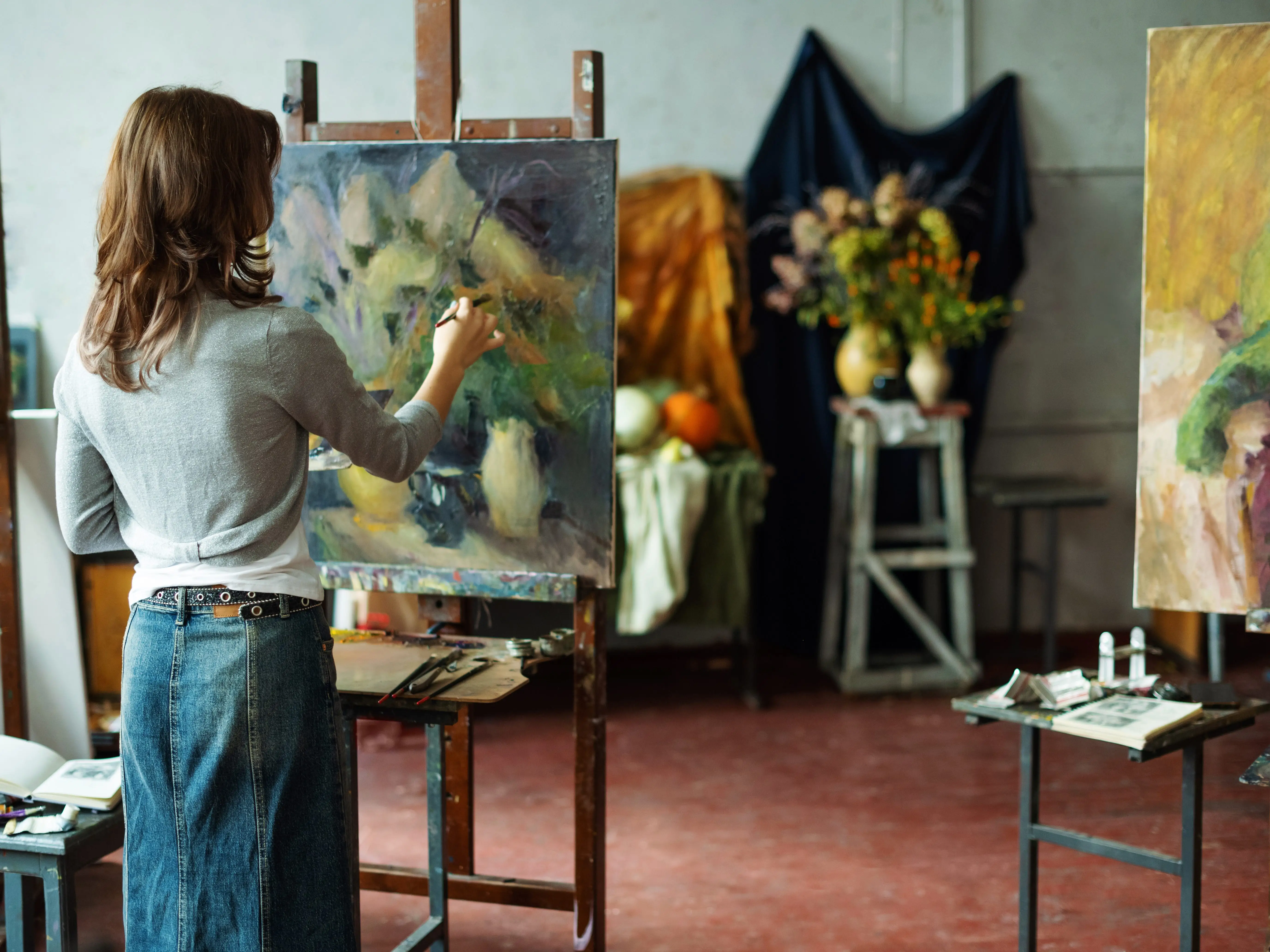 Portrait of teenage girl in painting class, art studio, art workshop. She paints still life on canvas with oil paints, holds brush, palette. Studying painting in college. stock photo