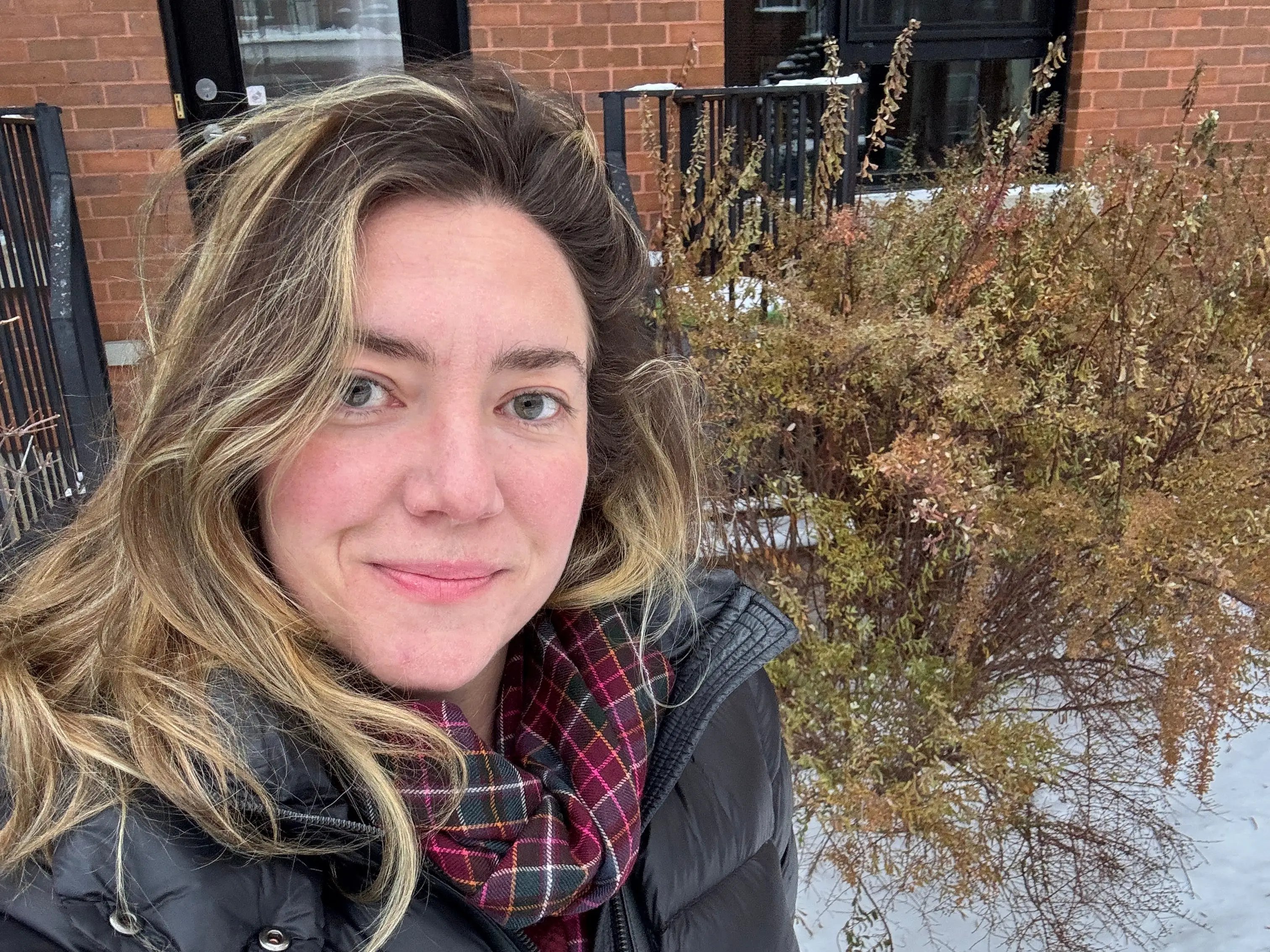 A woman with snow in the background and a brick wall.