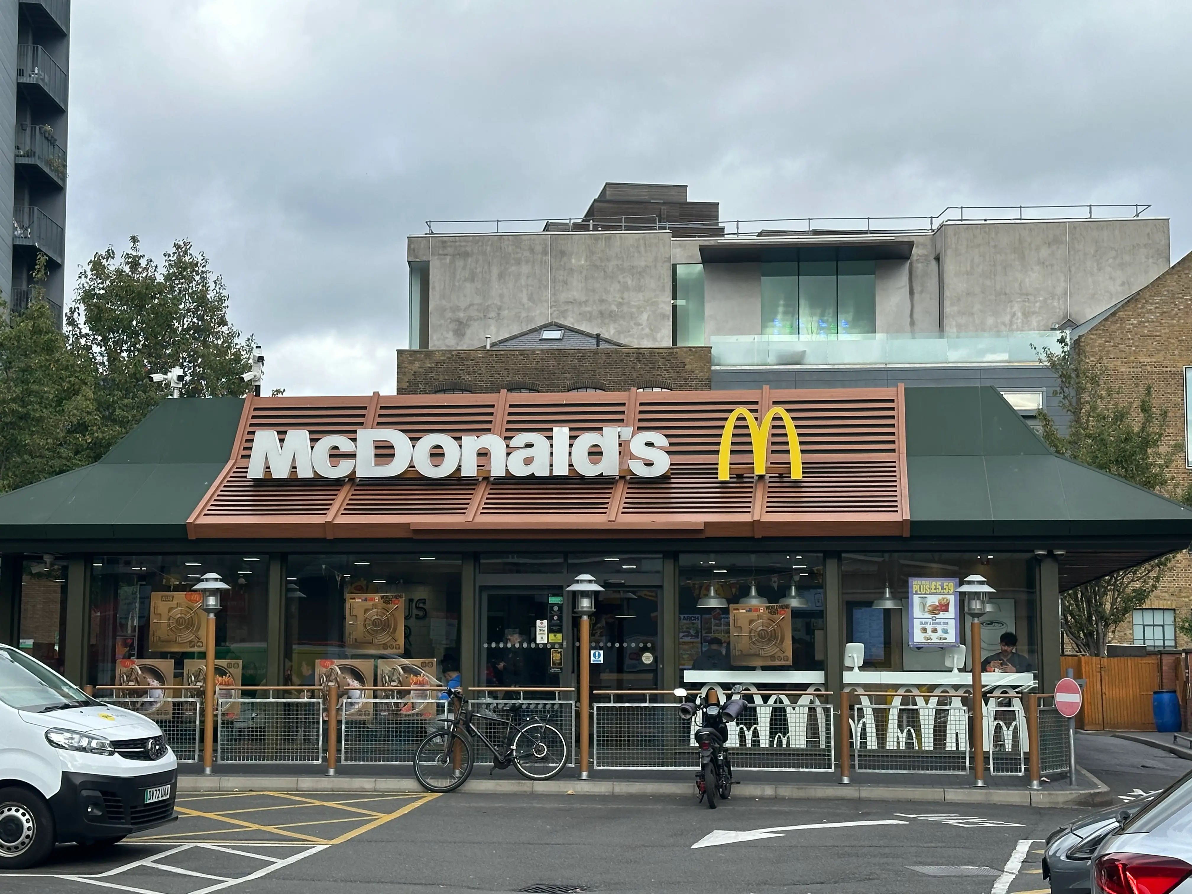 McDonald's restaurant exterior on a city street with parked bicycles, vehicles, and cloudy sky above.