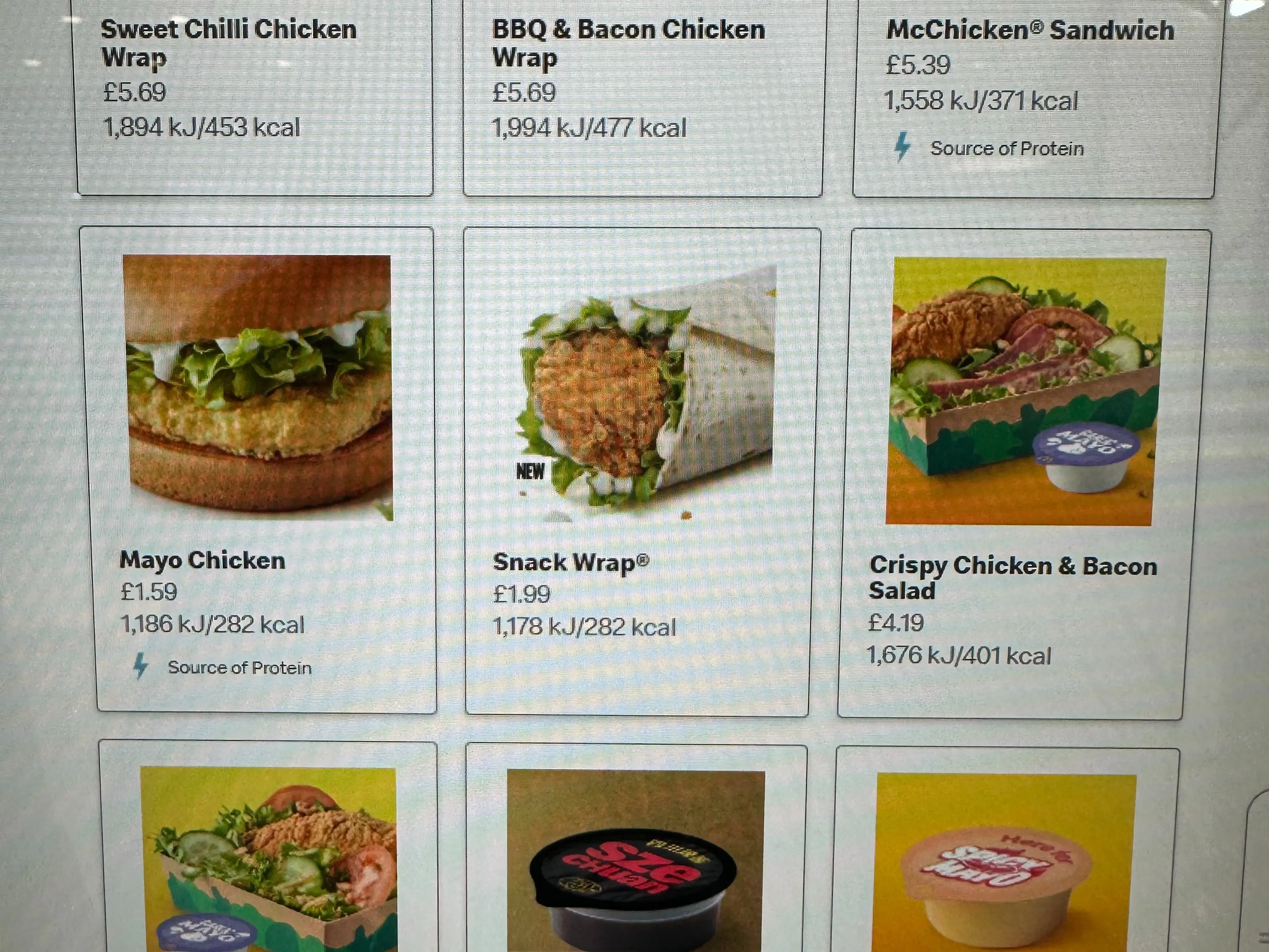 Digital fast-food menu screen showing chicken wraps, sandwiches, salad, prices, calories, and product photos.