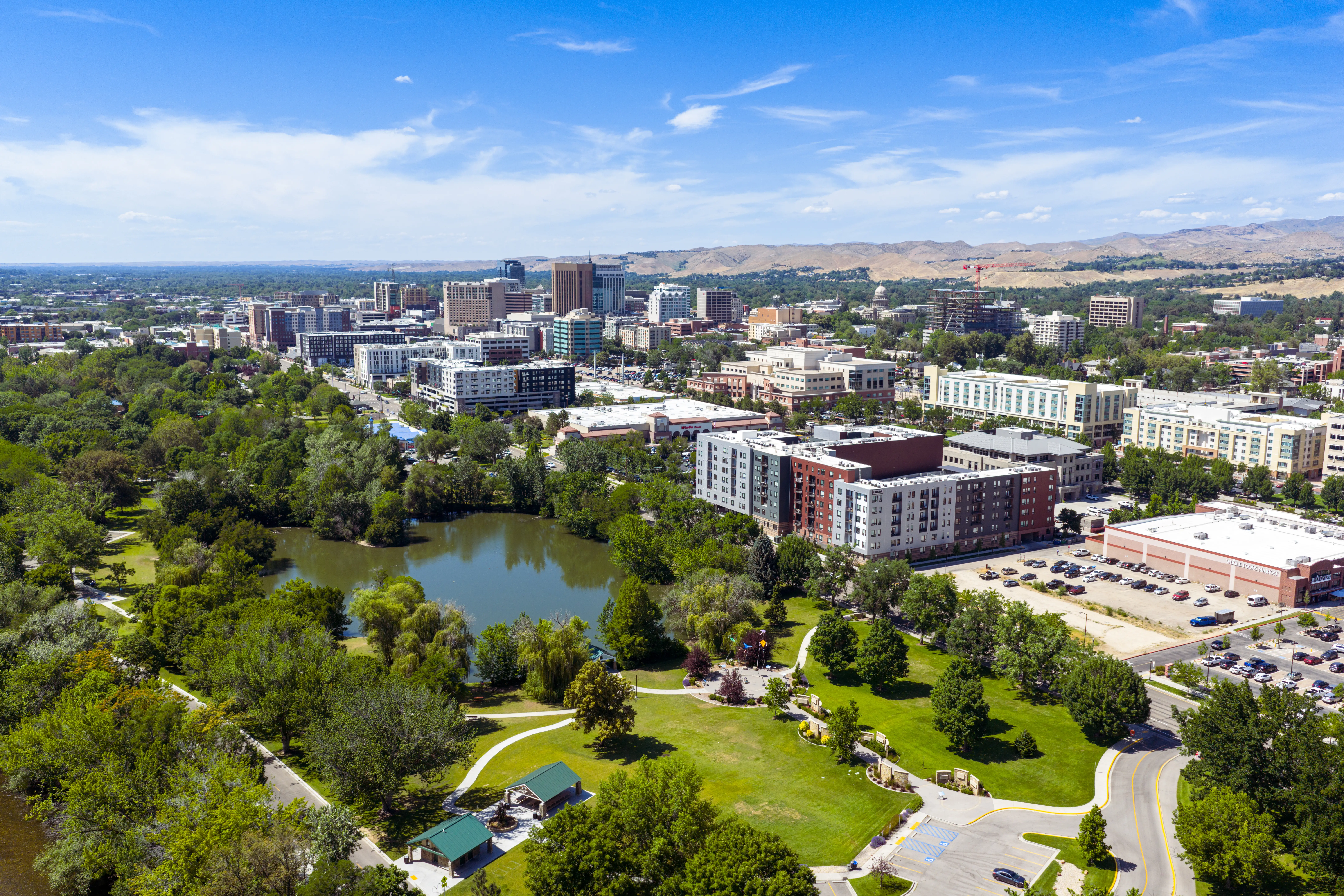 Aerial view of a downtown district beside a green park with ponds, roads, and distant hills.
