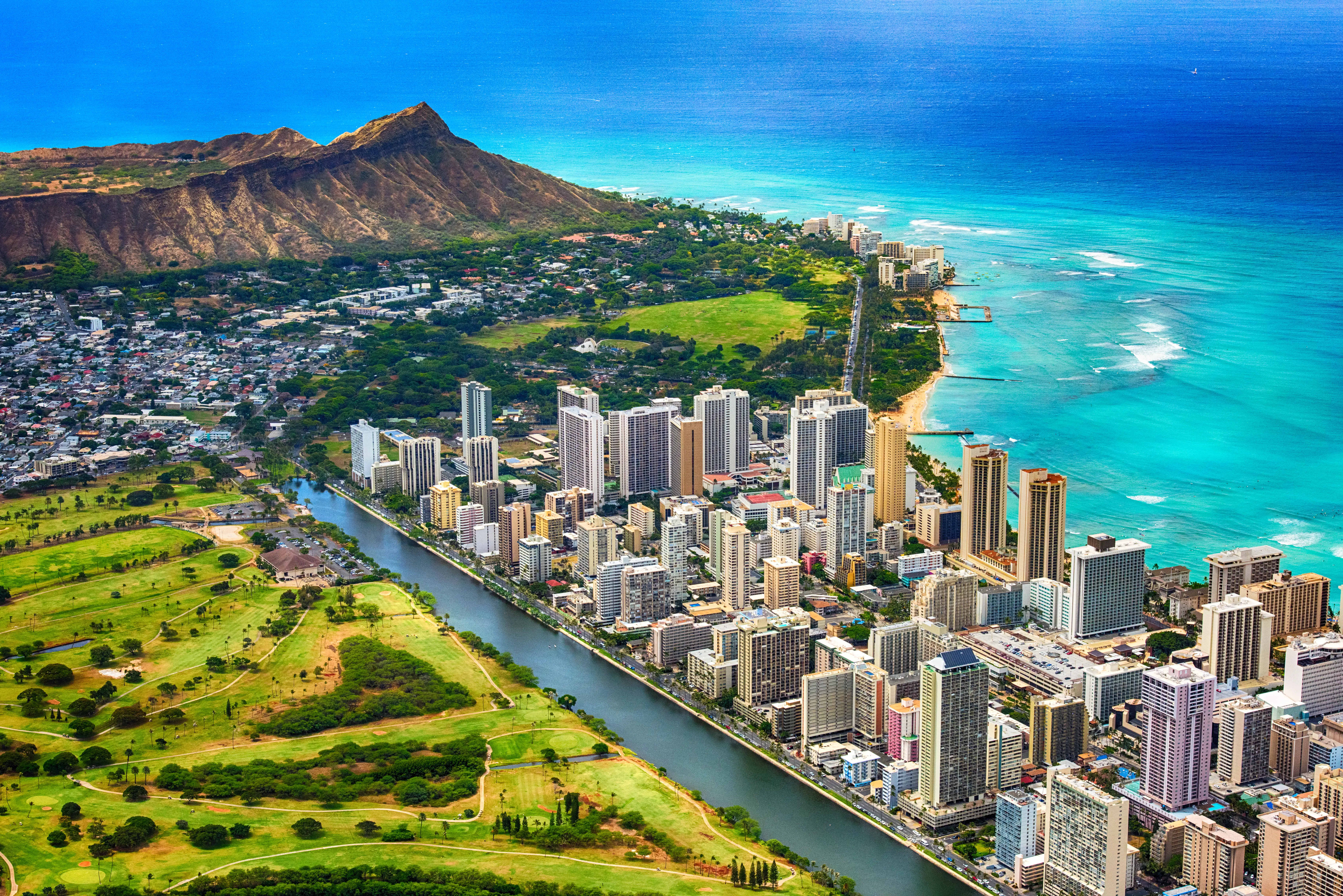 Aerial view of Waikiki high-rises, Ala Wai Canal, Diamond Head, and turquoise ocean in Honolulu.