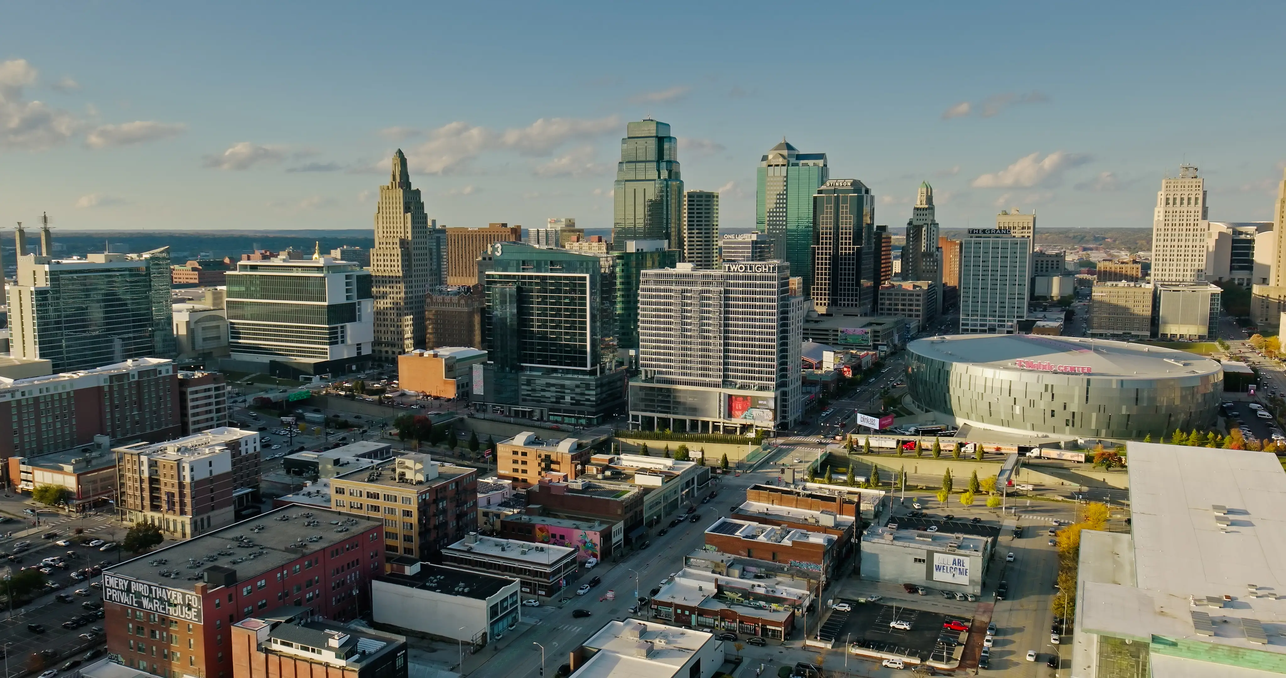 Downtown Kansas City skyline with high-rise buildings and the T-Mobile Center arena under a clear sky.