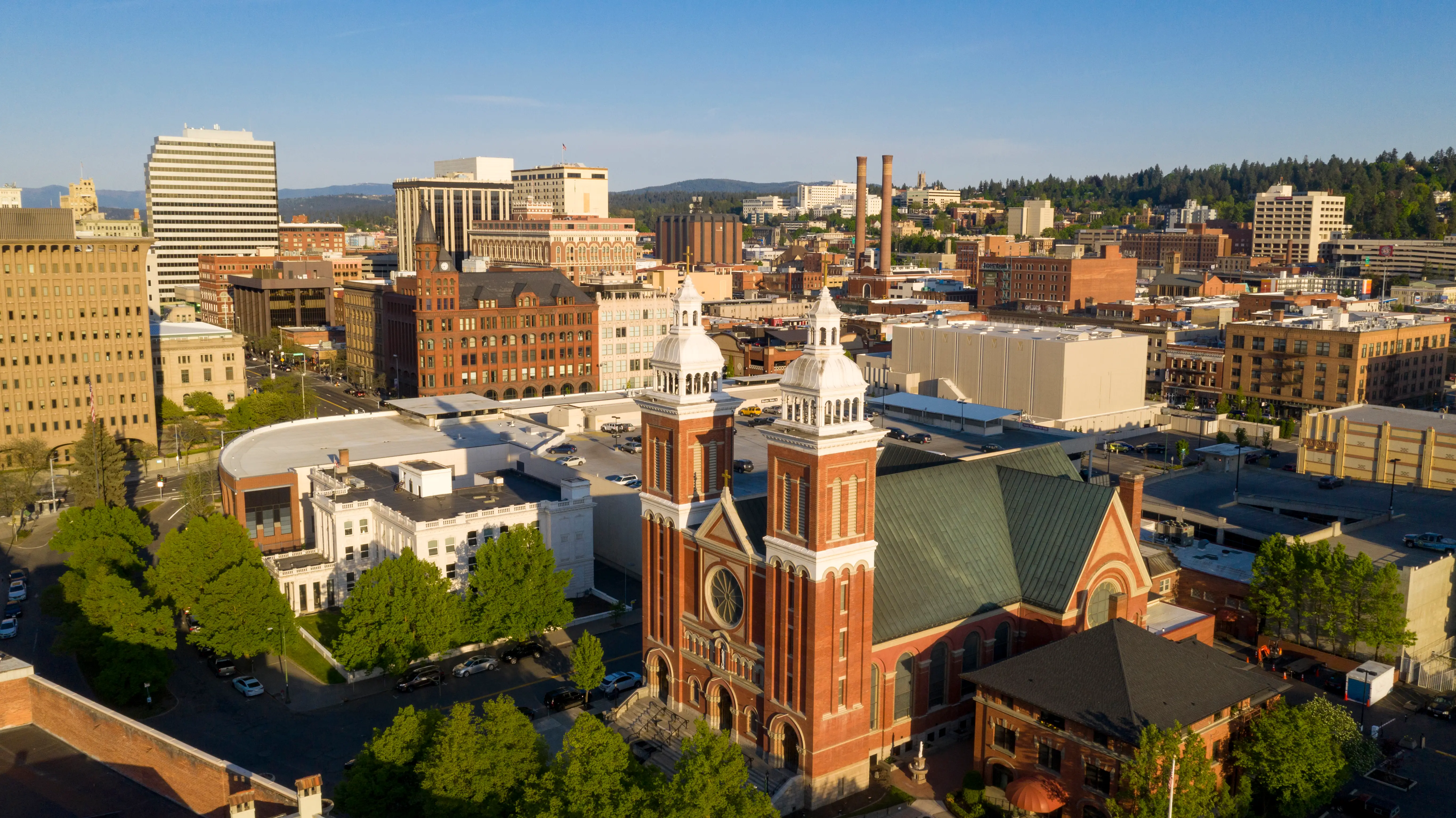 Aerial view of a downtown skyline with a prominent red brick church, office buildings, trees, and clear sky.
