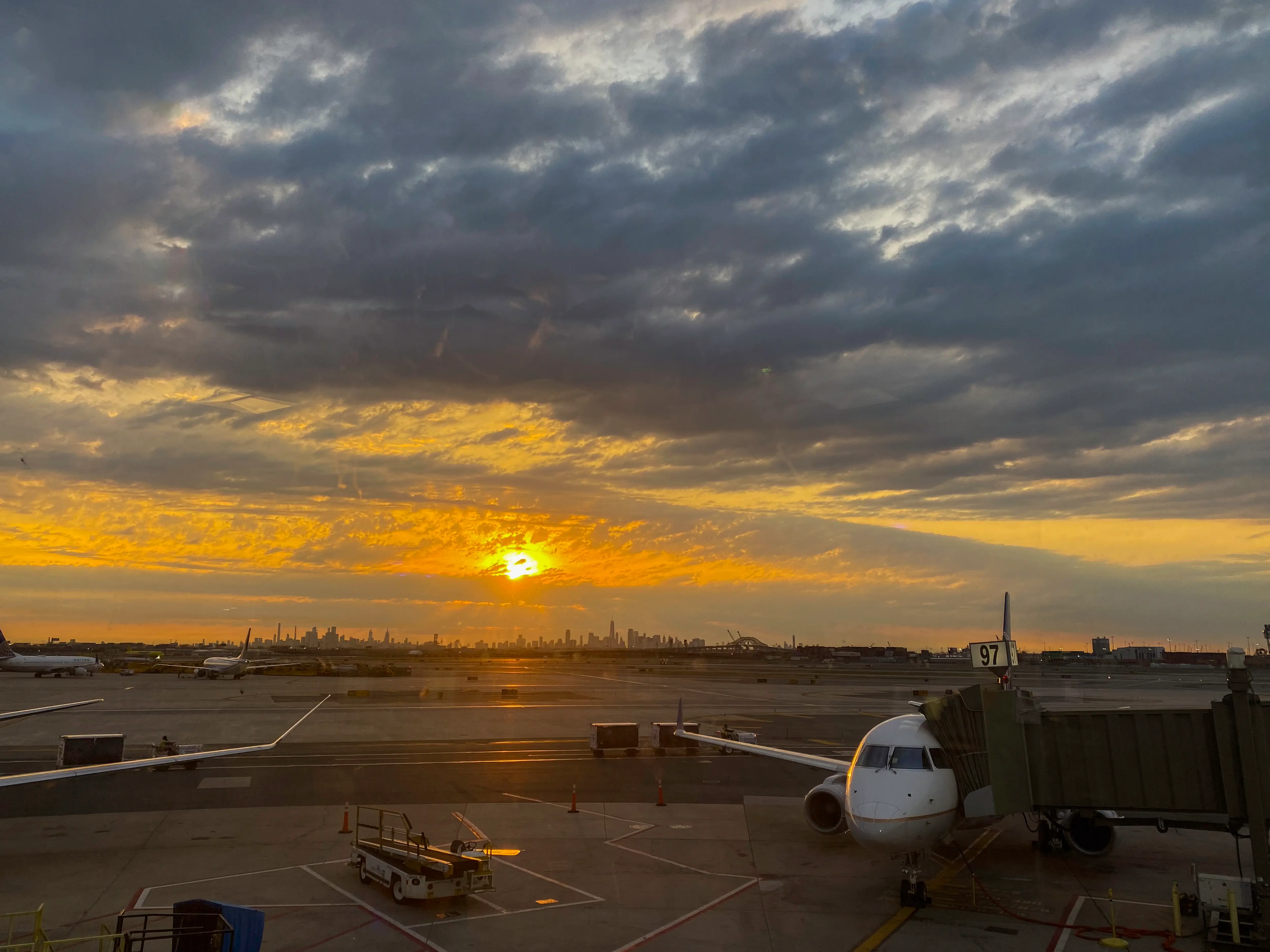 Commercial airplane parked at an airport gate during a sunrise over a distant city skyline.