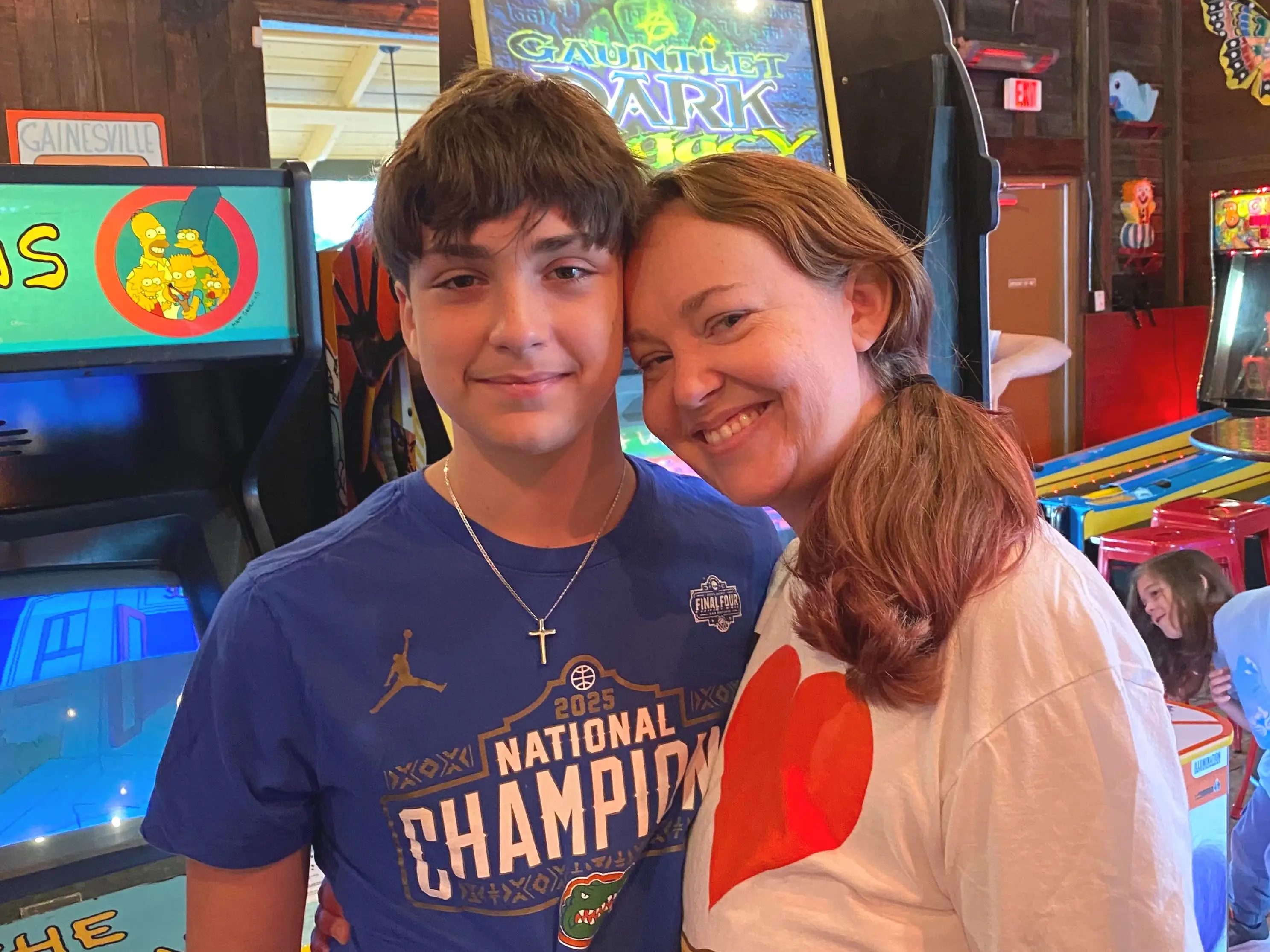 Two people smile and pose together among colorful arcade machines, including The Simpsons and Gauntlet Dark Legacy cabinets.