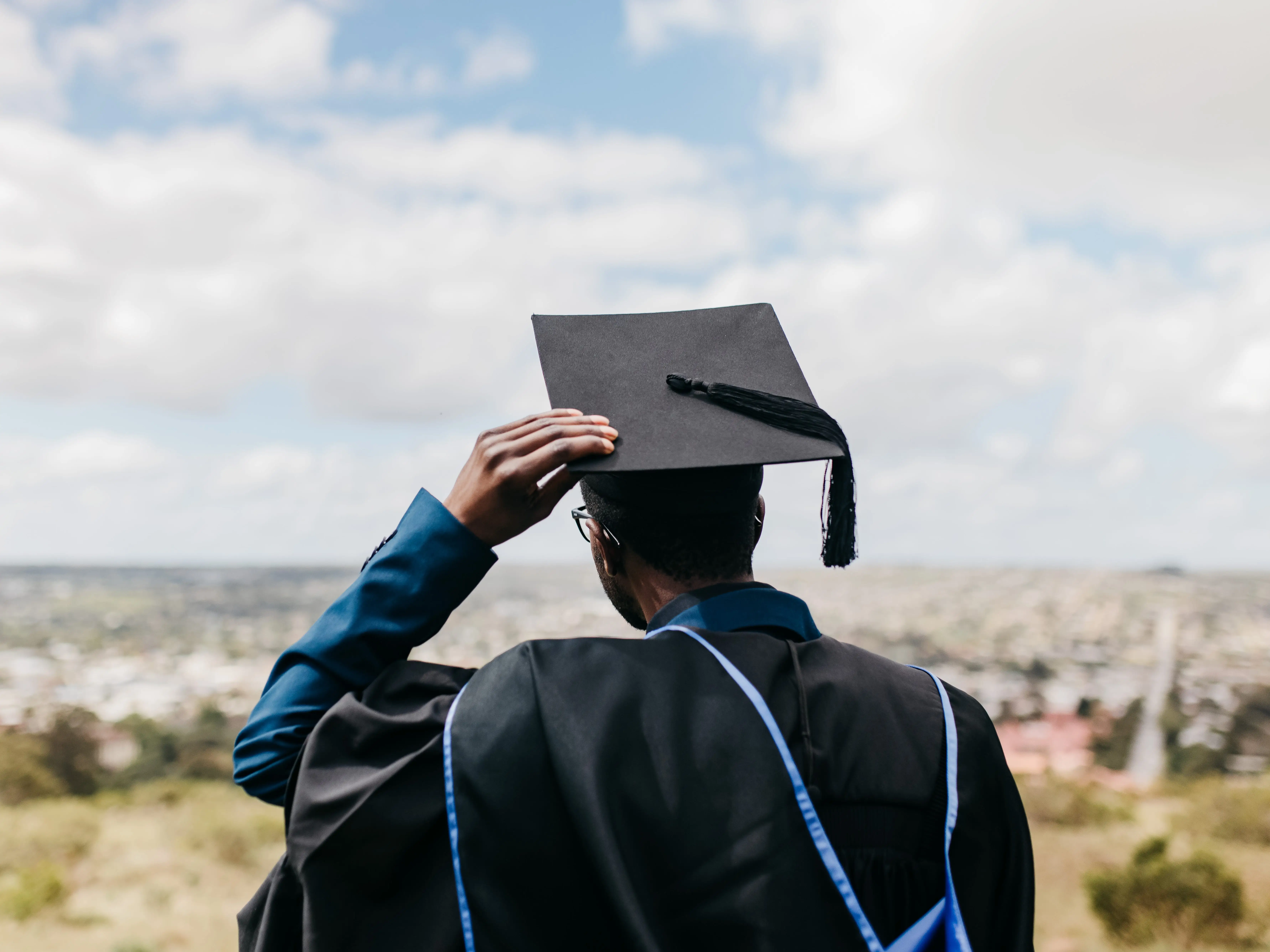 A male graduate wearing a graduation gown and holding onto mortarboard.