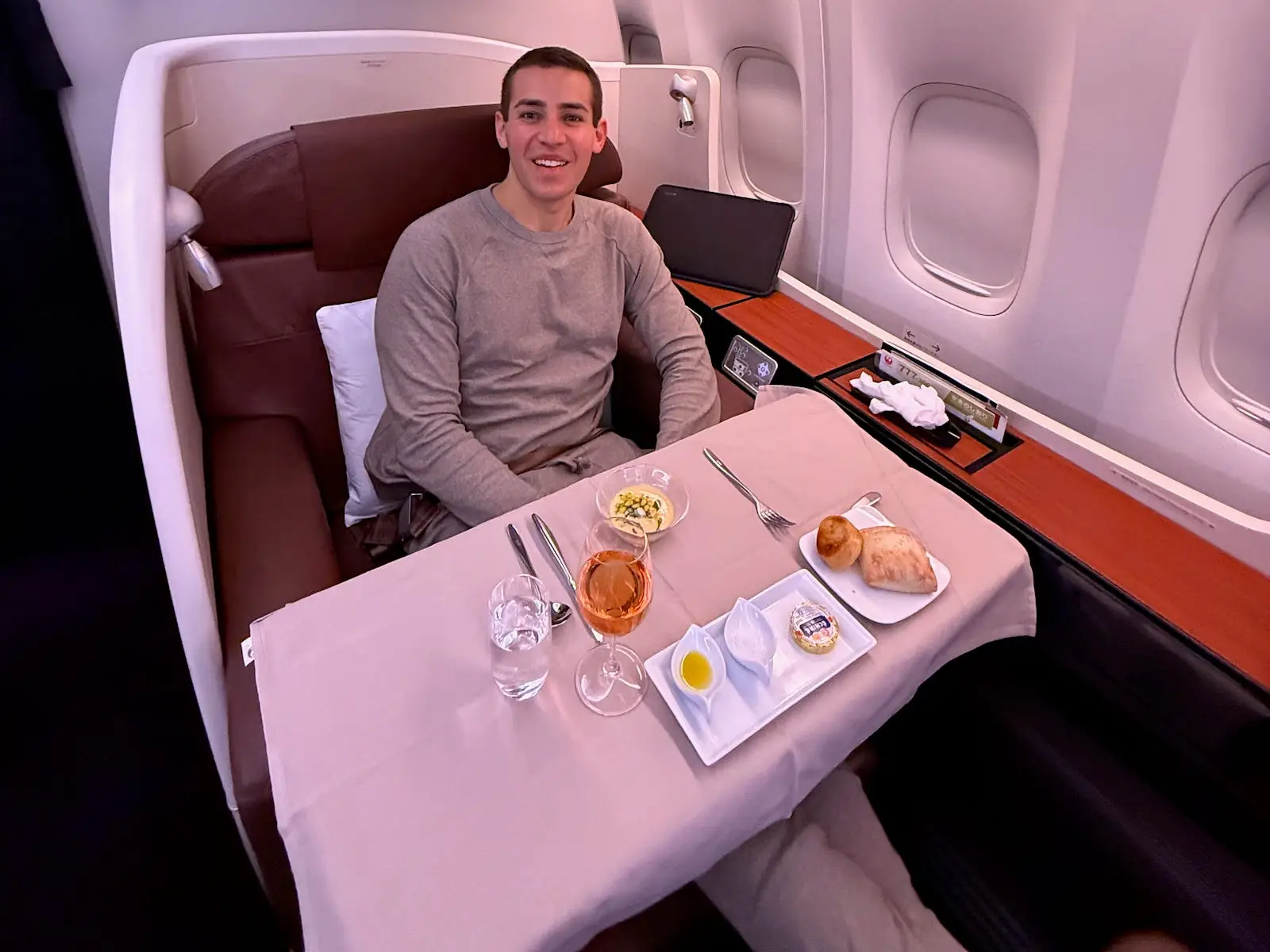 Passenger seated in a private aircraft suite with a tray table meal and drinks beside cabin windows.