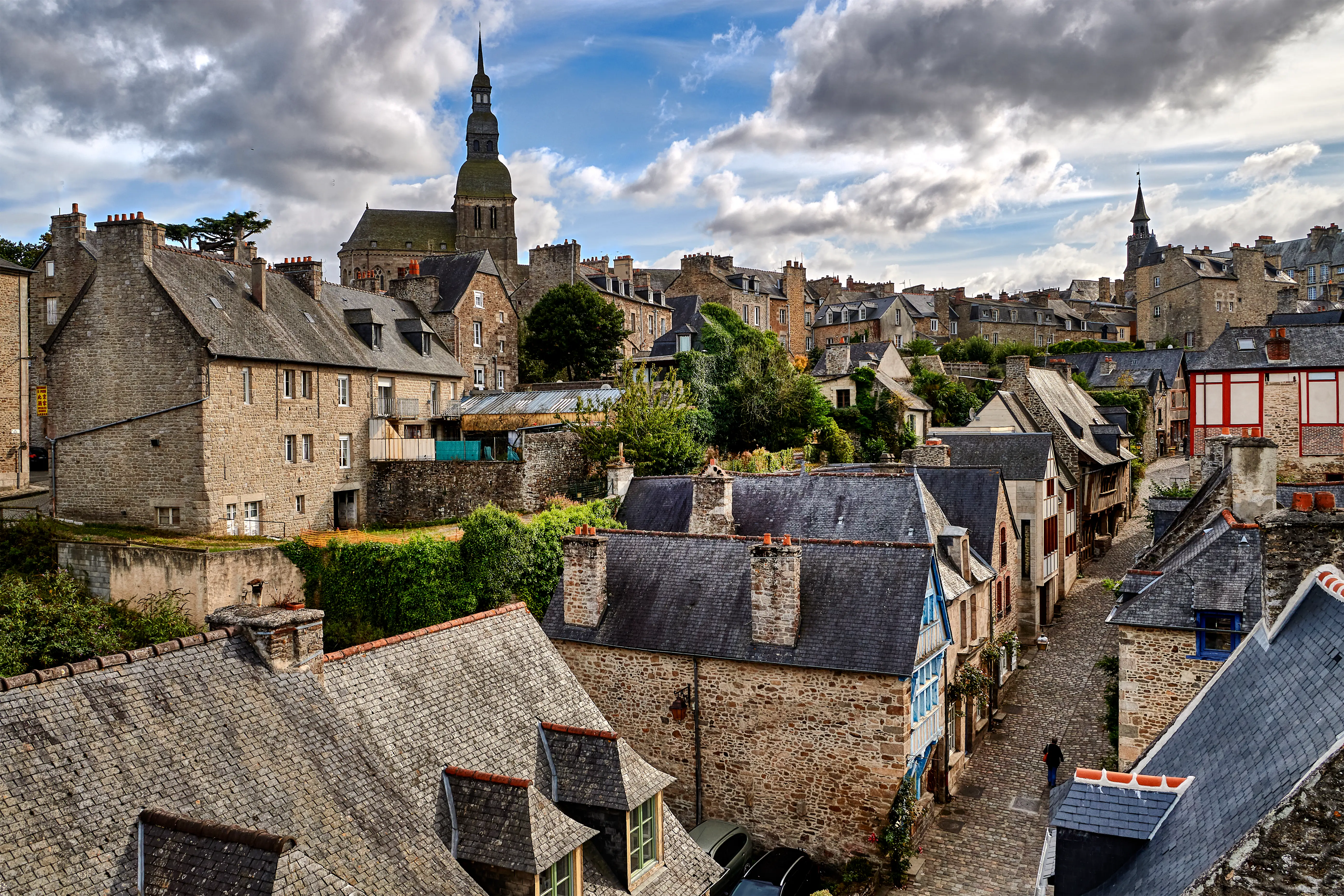 Stone homes lined up on a street, a tall cathedral stands tall in the background.