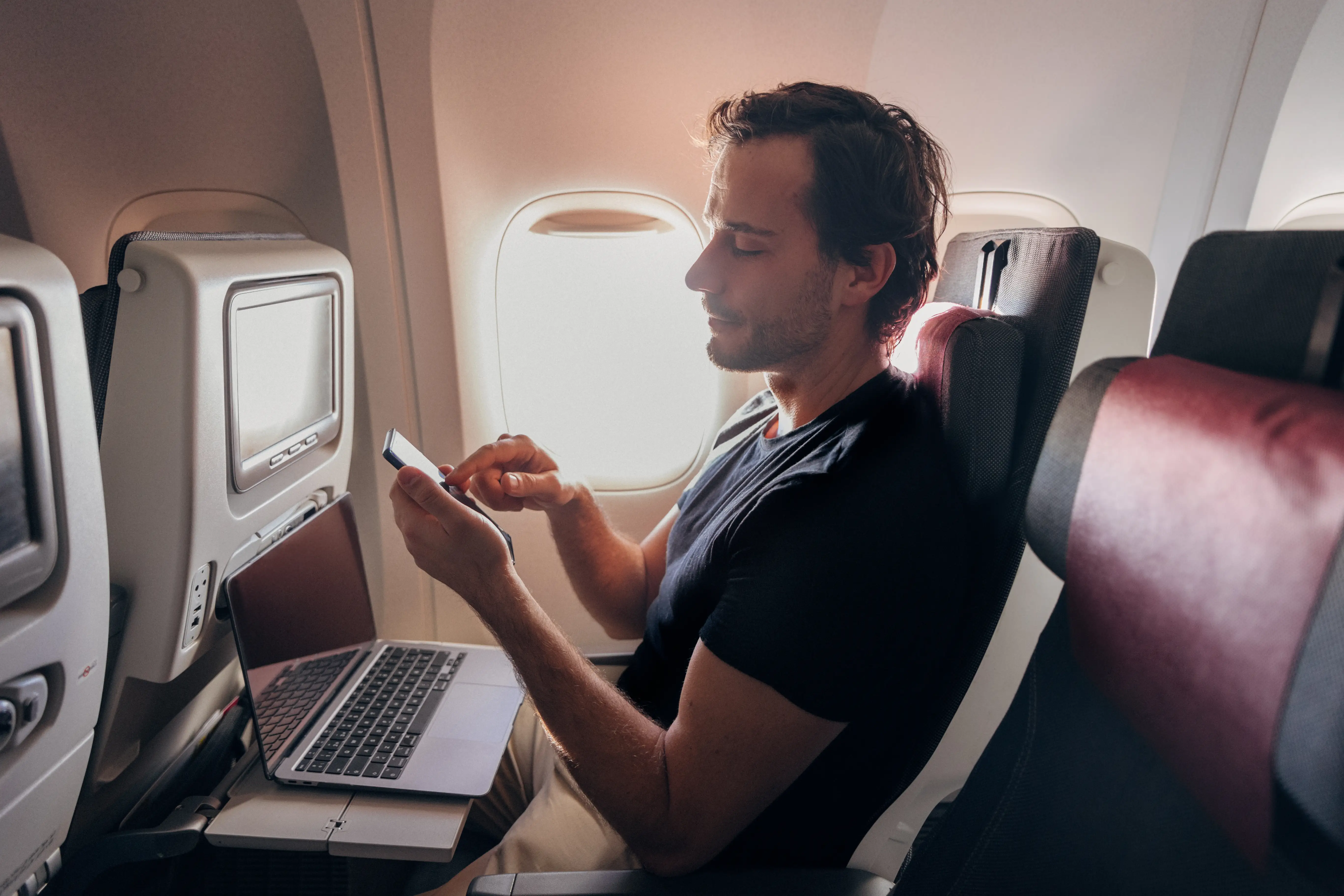 A man using a phone and laptop on a flight.