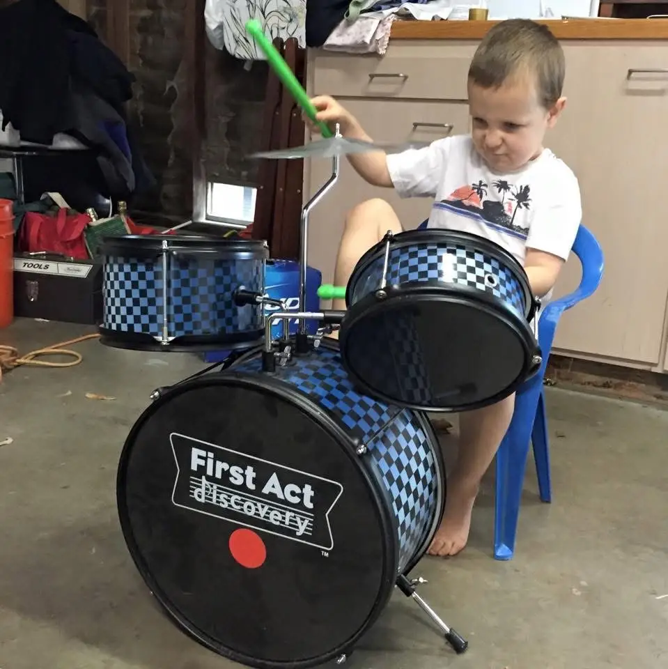 A child plays a blue checkered First Act discovery drum set in a garage.