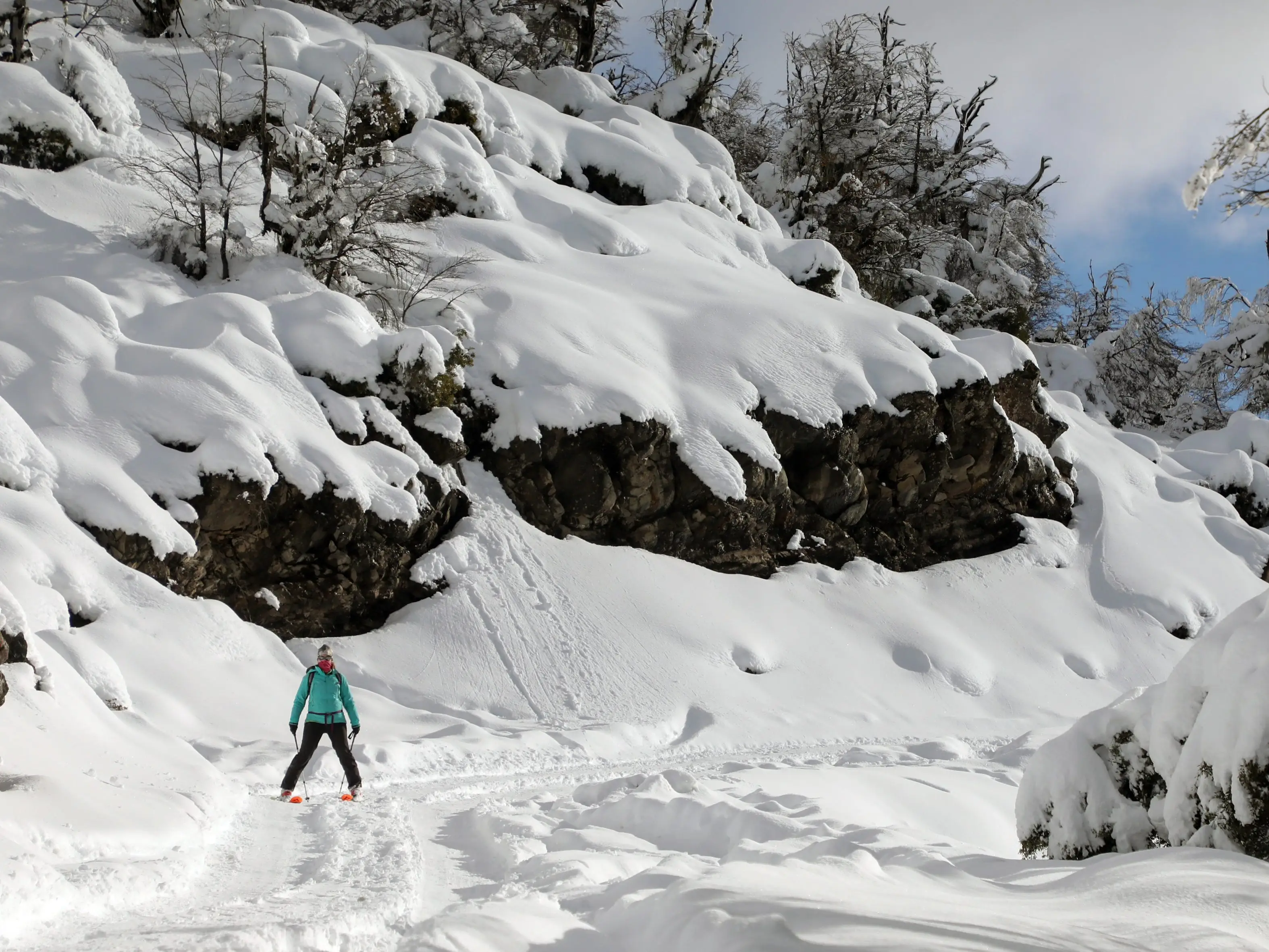 A woman skiis next to a hill packed with snow.