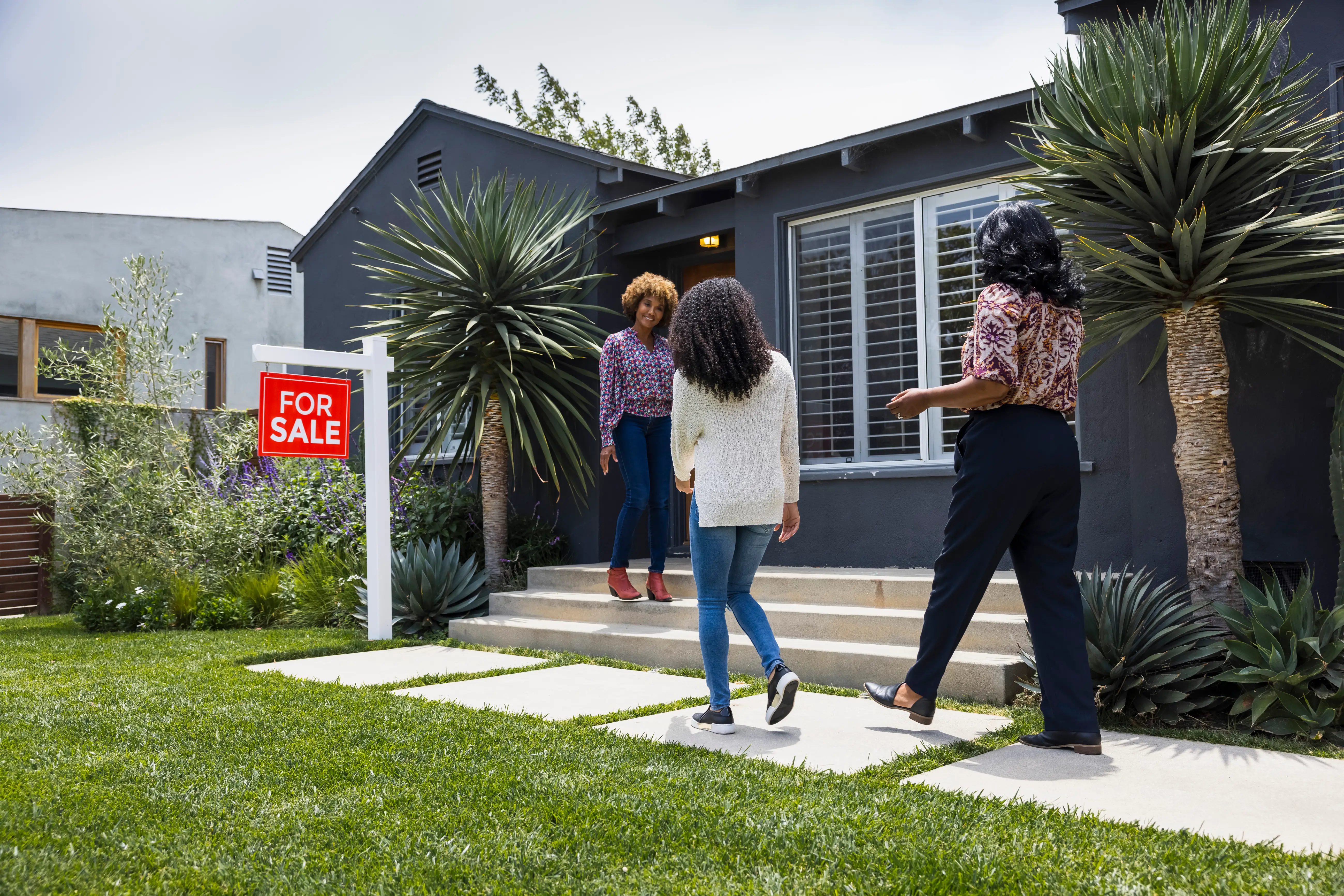Three people are outside a house with a visible 