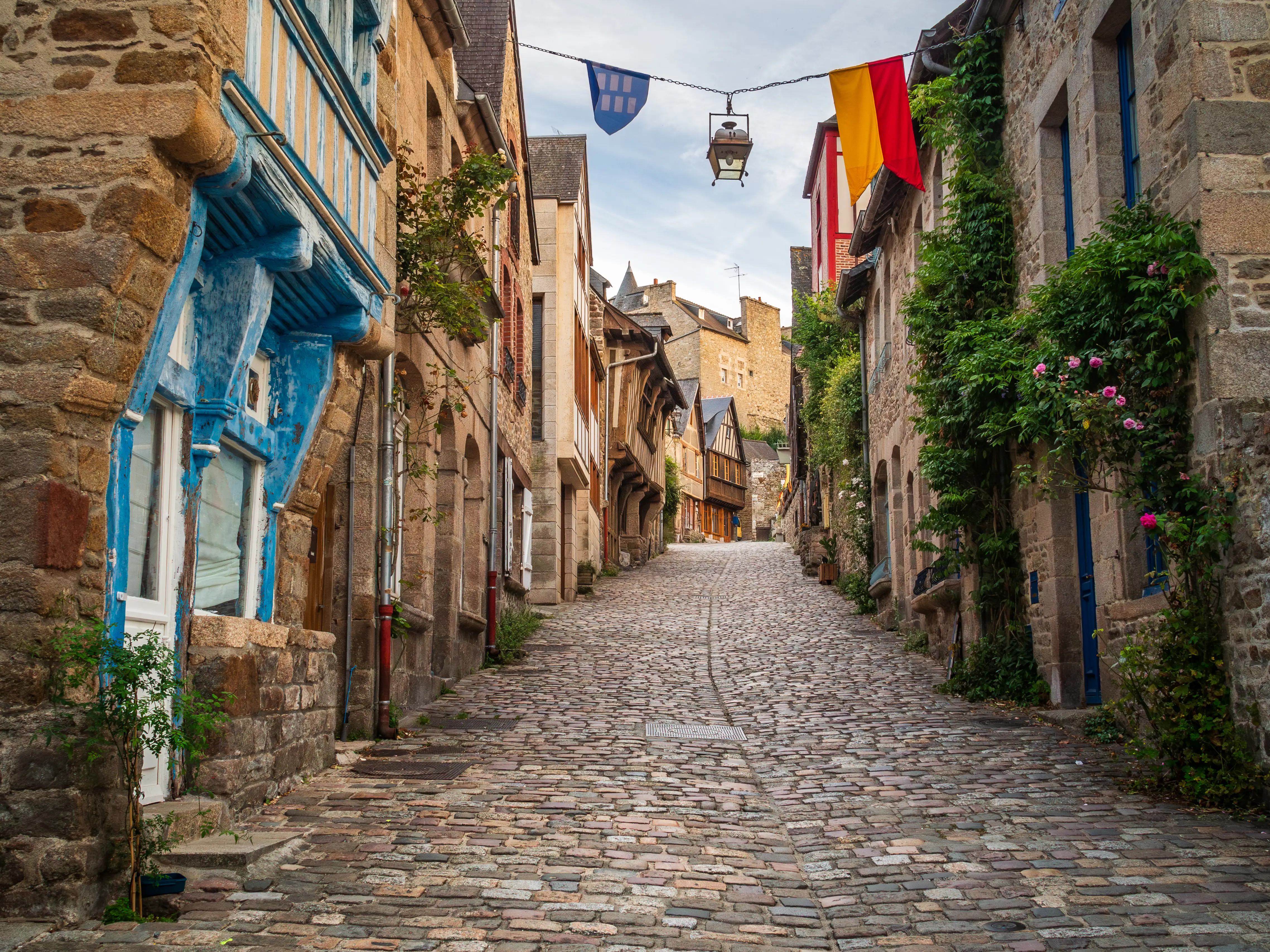 An uphill cobblestone street in the medieval old town of Dinan with several traditional Breton granite and half-timbered houses.