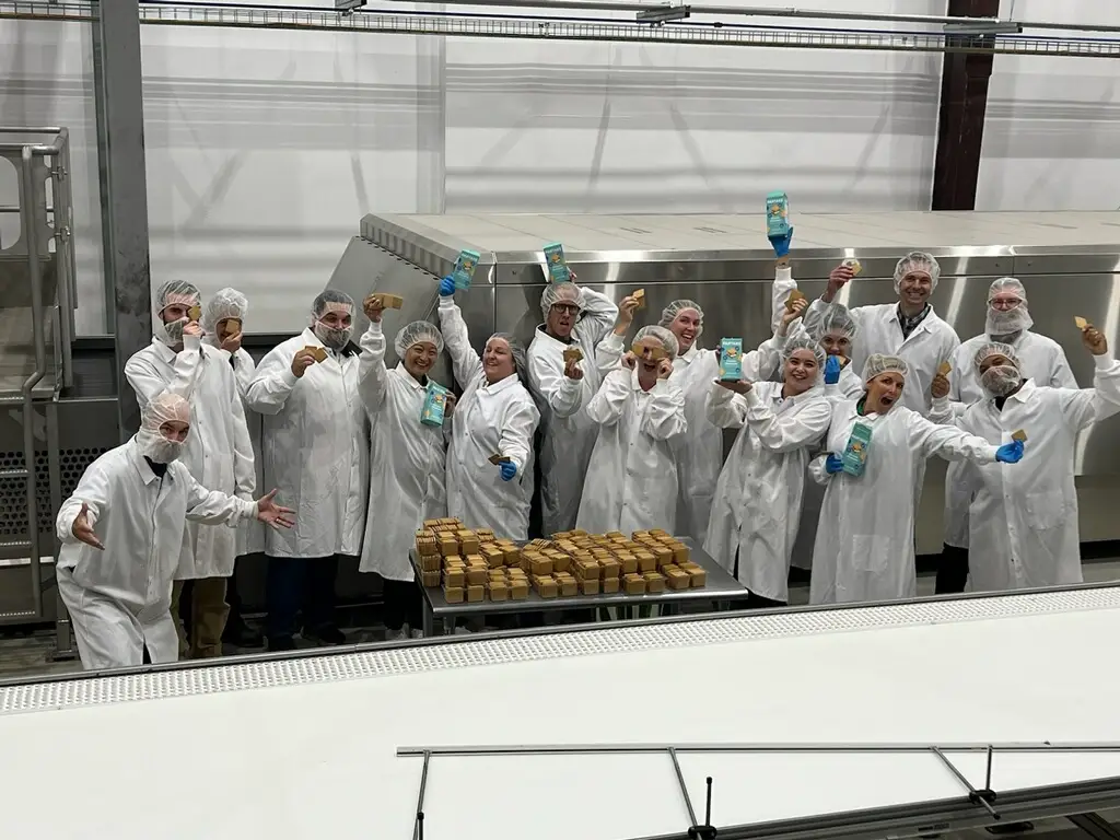 Denise Woodard and team in white lab coats and hairnets in an assembly line kitchen.