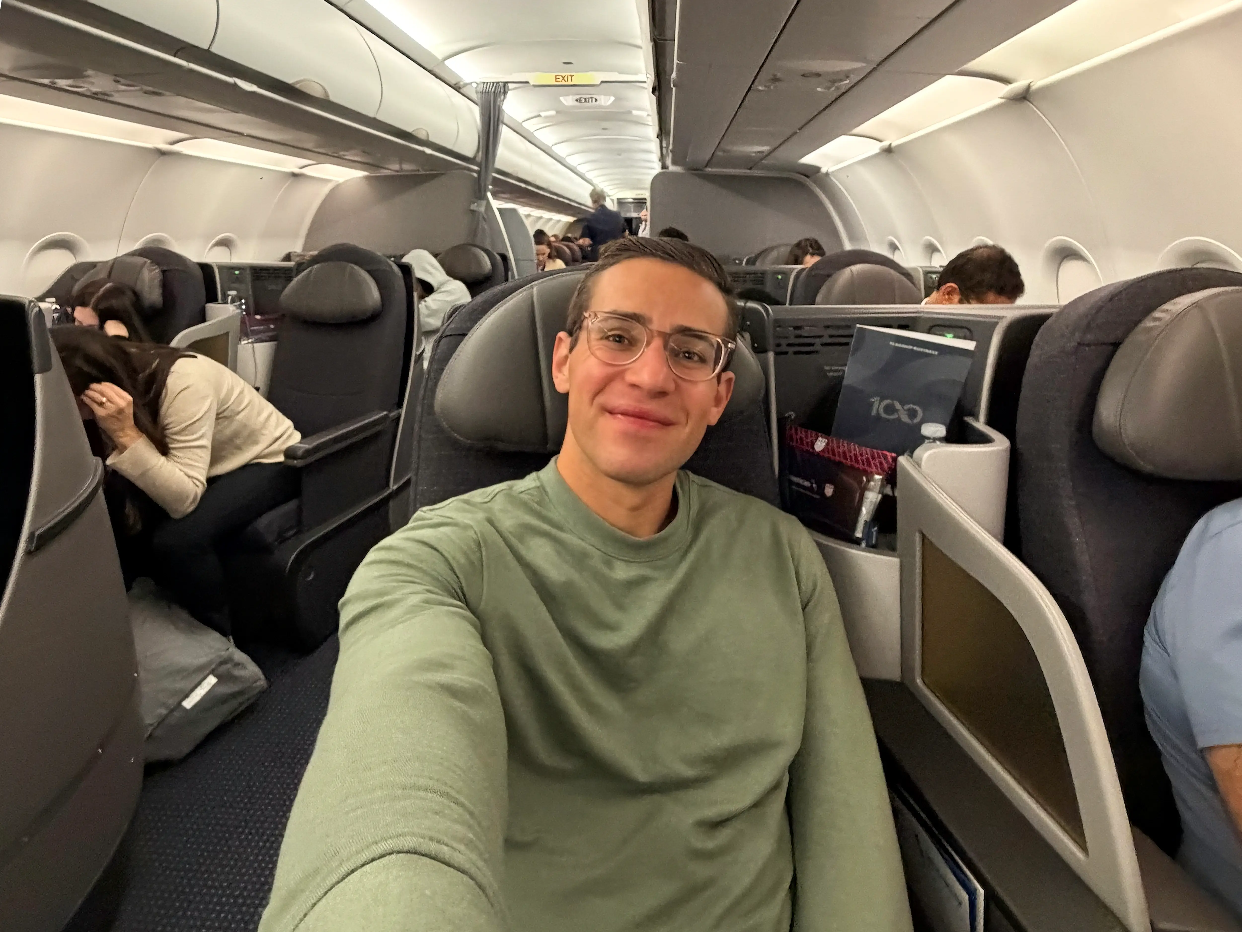Smiling passenger takes a selfie from a premium airplane seat inside a crowded cabin.
