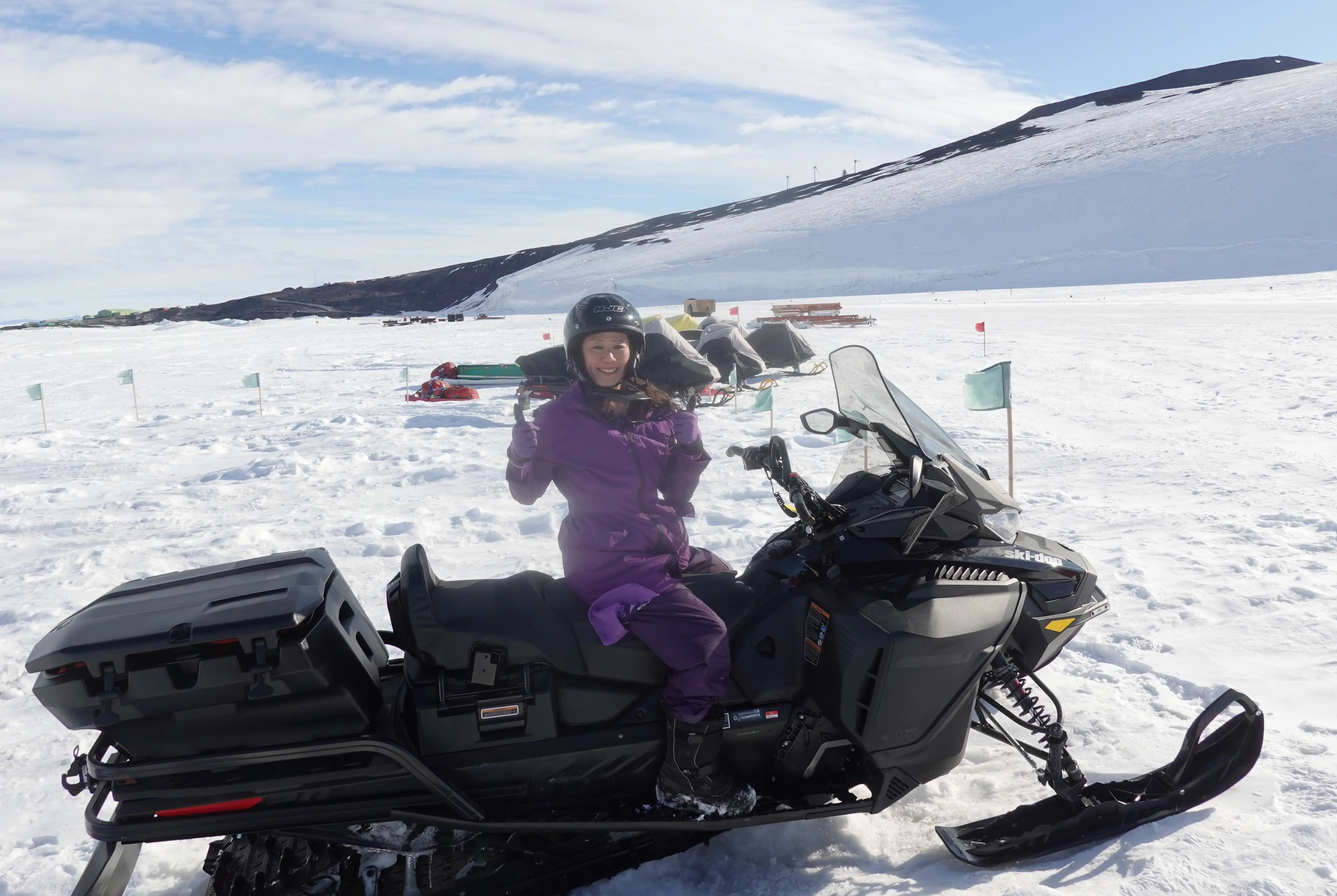 Helmeted rider in a purple snowsuit sits on a black snowmobile in a snowy mountain landscape.